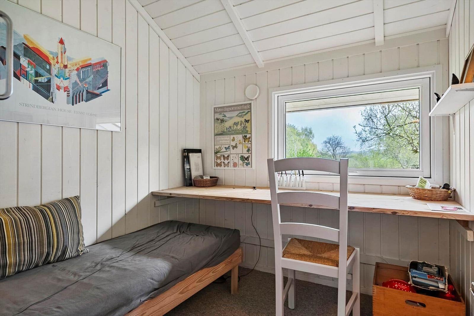 Schlafzimmer mit Bett, Schreibtisch und Fensterblick auf Bäume.