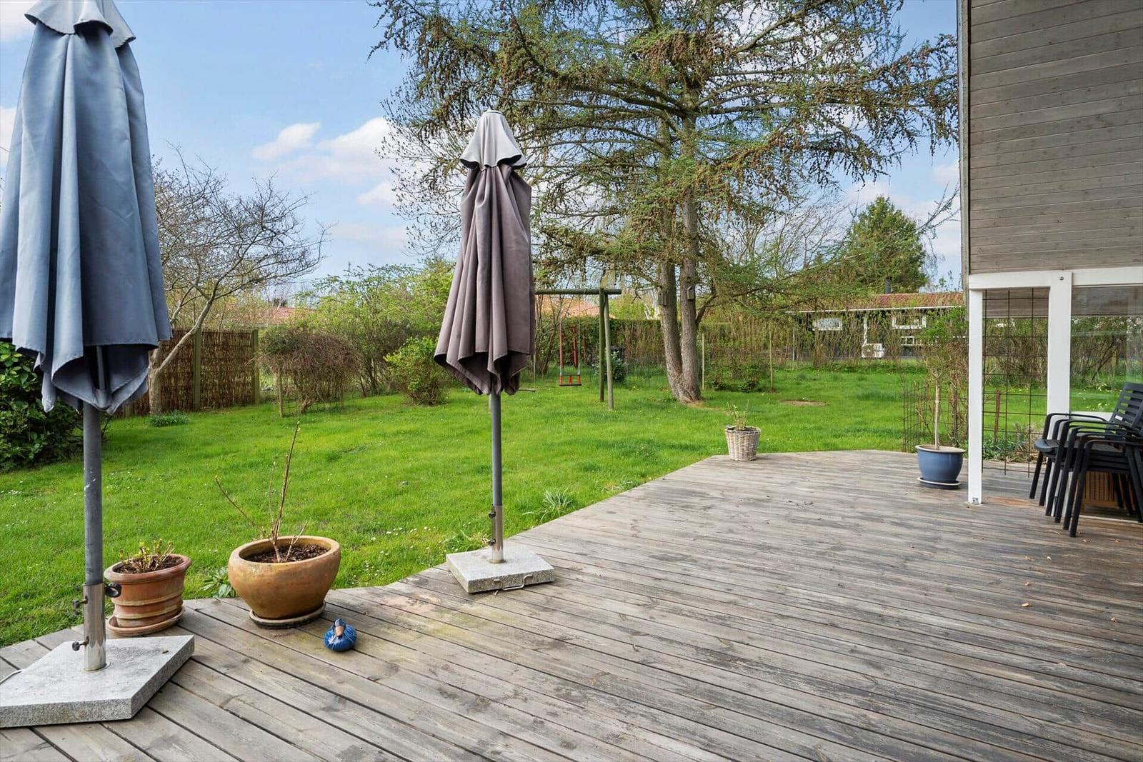 Terrasse mit zwei geschlossenen Sonnenschirmen und Garten im Hintergrund.