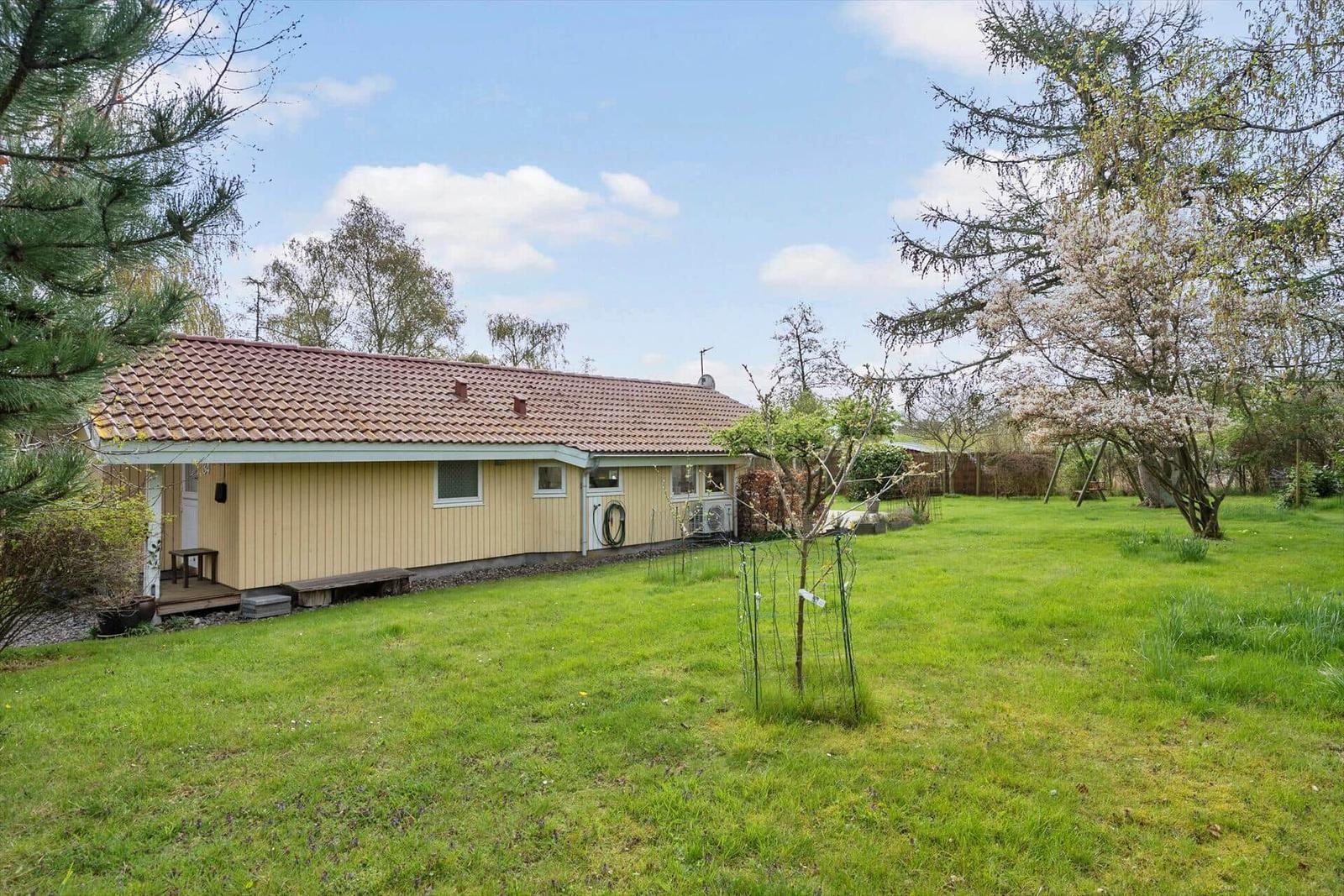 Ein gelbes Haus mit braunem Dach und großem Garten mit Bäumen und Rasen.
