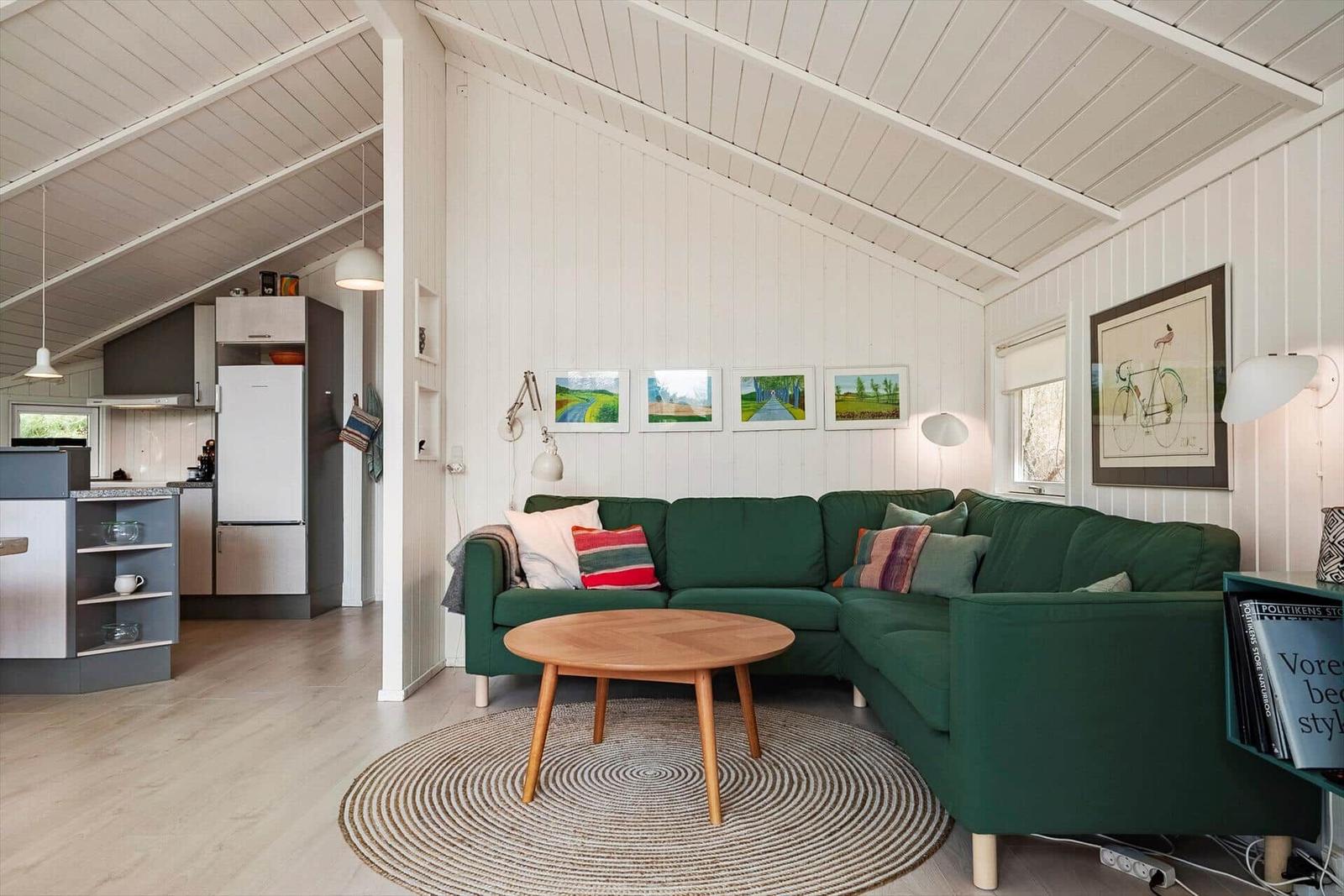 Ein Wohnzimmer mit grünem Sofa, runden Tisch und weißen Wänden. Küche im Hintergrund.