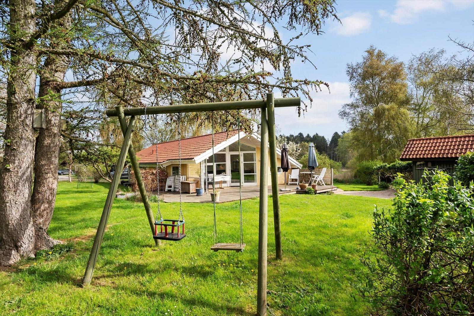 Haus mit Garten, Schaukel und Terrasse unter Bäumen.