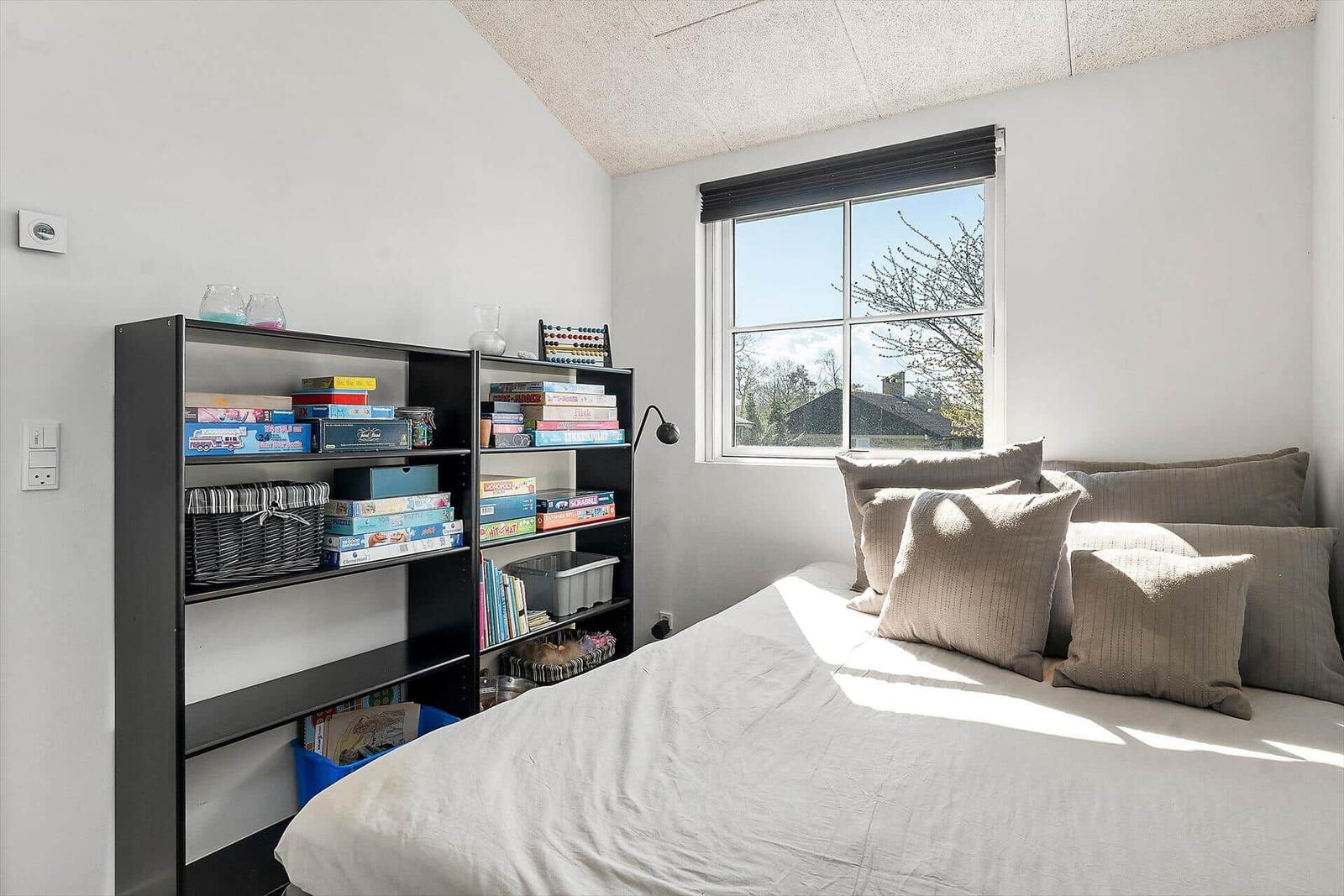 Schlafzimmer mit Bett, Fenster und Bücherregal.