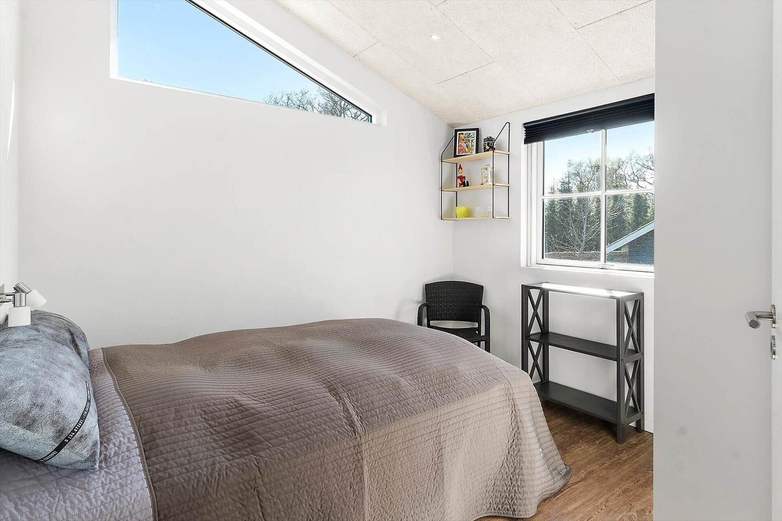 Schlafzimmer mit Bett, Fenster und Schrank. Blick auf Bäume und Himmel.