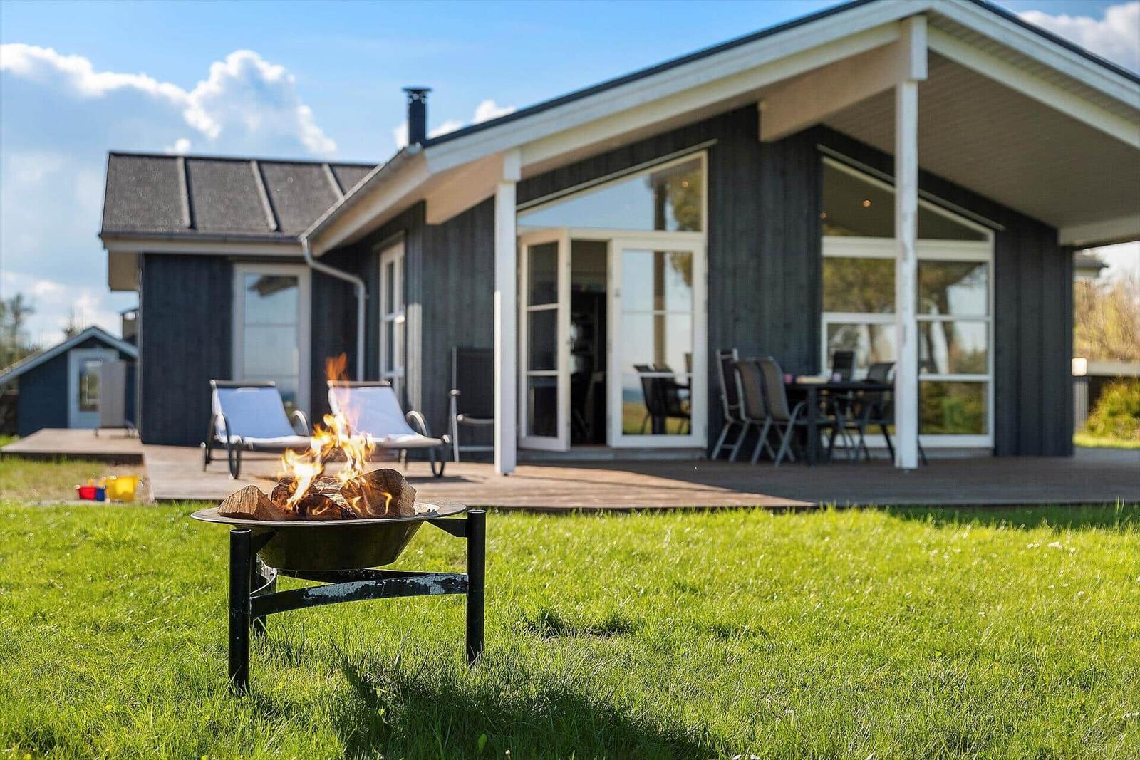 Haus mit Terrasse, Garten und brennendem Feuerkorb.