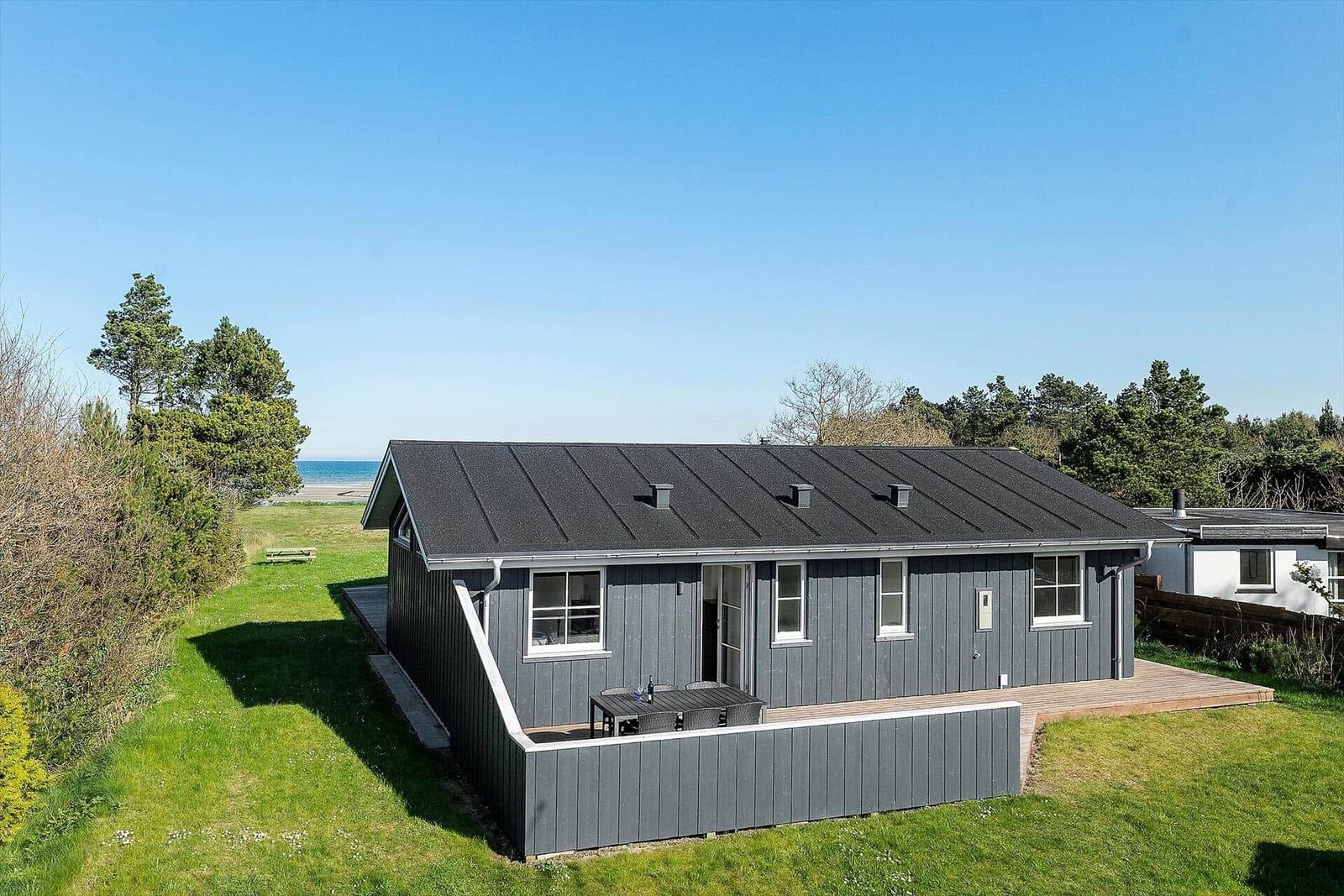 Ein graues Ferienhaus mit Terrasse und Blick aufs Meer.