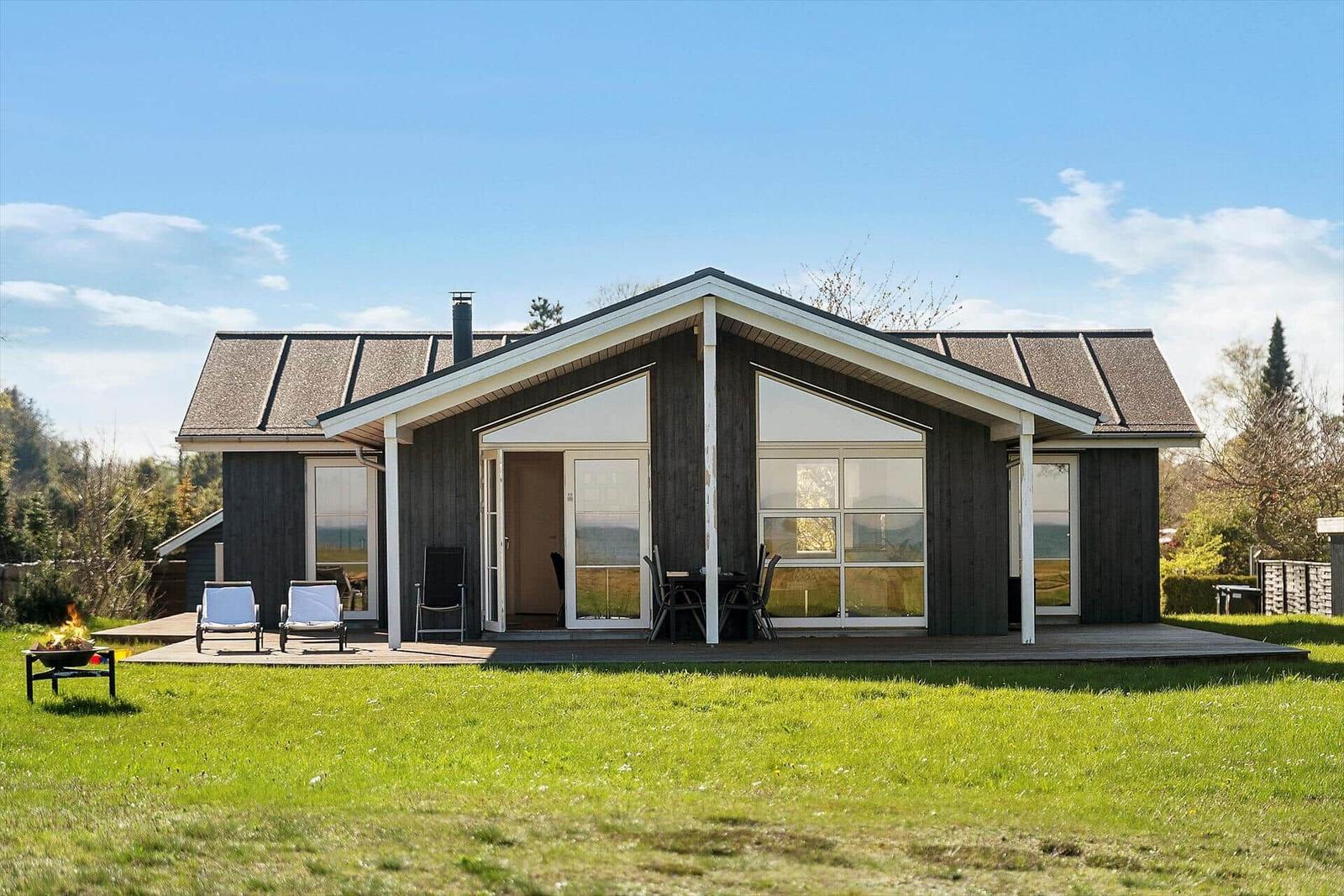 Moderne Holzhütte mit Terrasse, Sitzgelegenheiten und Grillplatz im Grünen.
