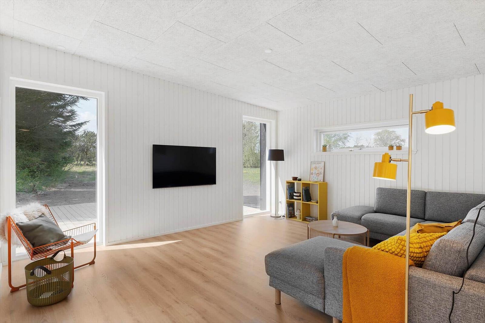 Wohnzimmer mit grauem Sofa, gelber Stehlampe und Fernseher an der Wand.