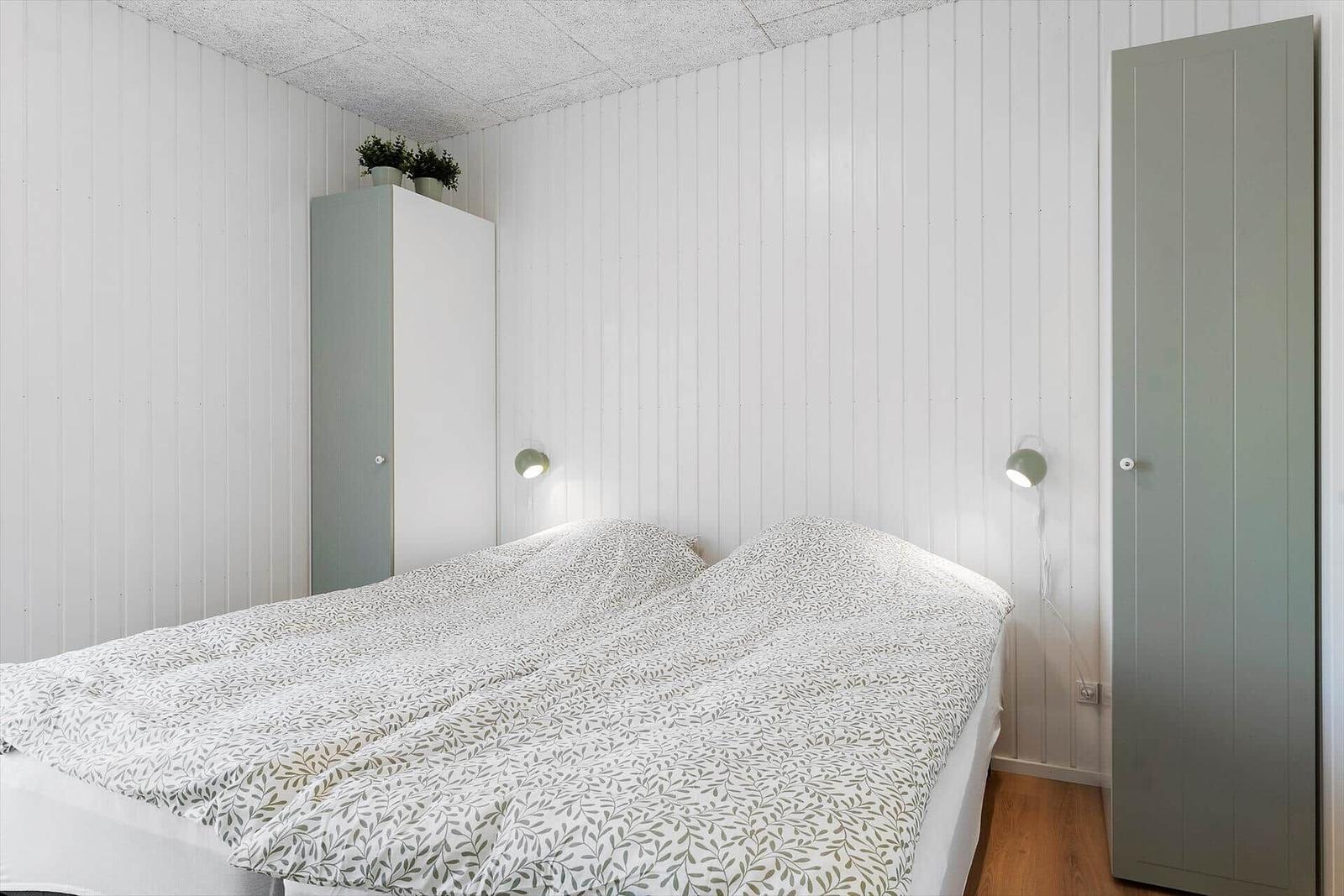 Schlafzimmer mit Bett, Kleiderschrank und Wandlampen.