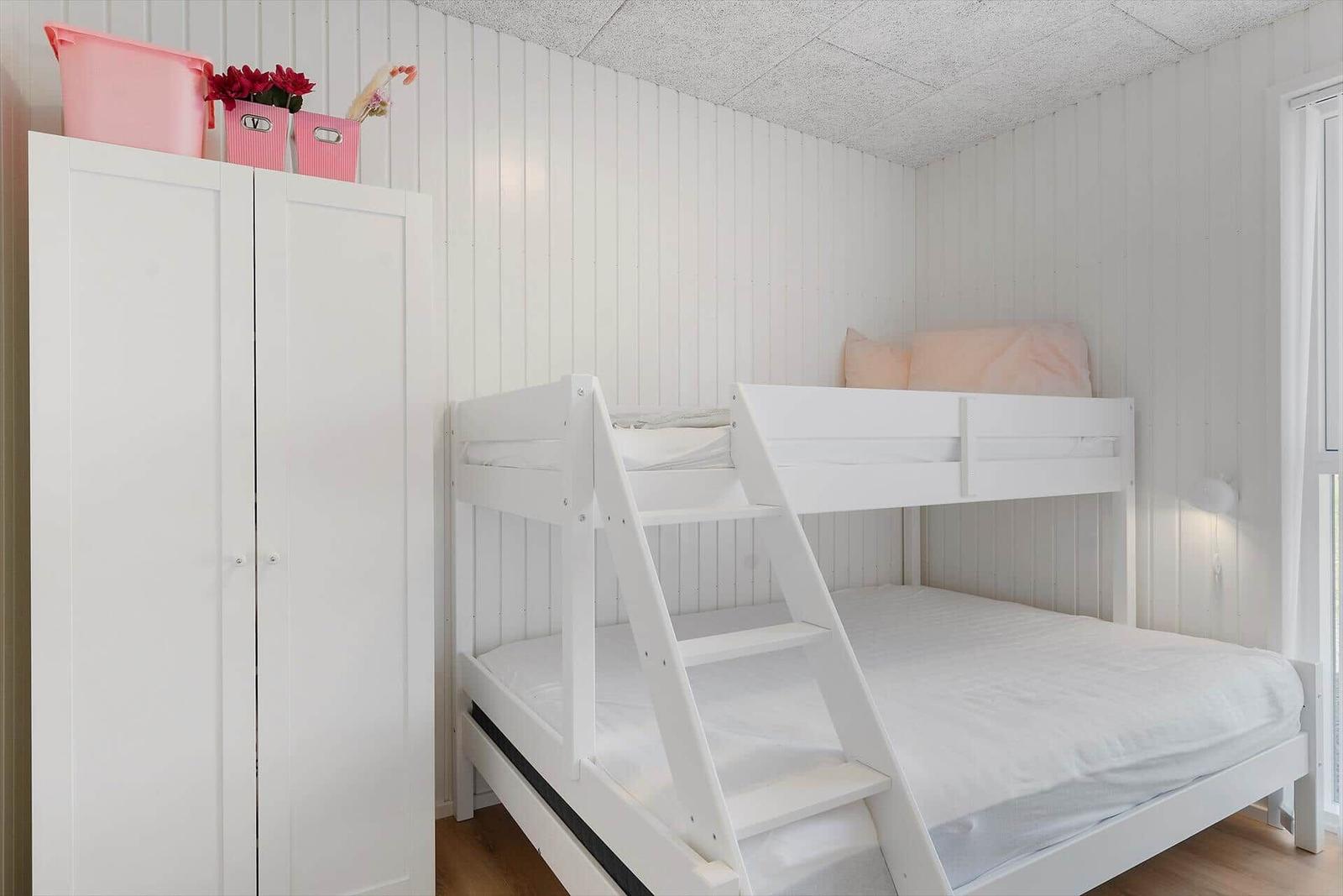 Schlafzimmer mit weißem Doppelstockbett und Kleiderschrank. Wandverkleidung und Holzboden.