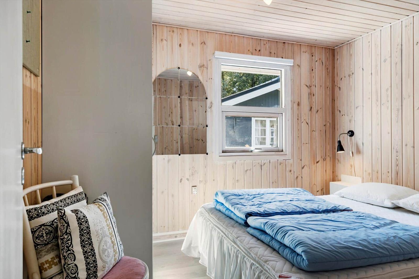 Schlafzimmer mit Holzwand, Bett mit blauer Decke und Fenster.
