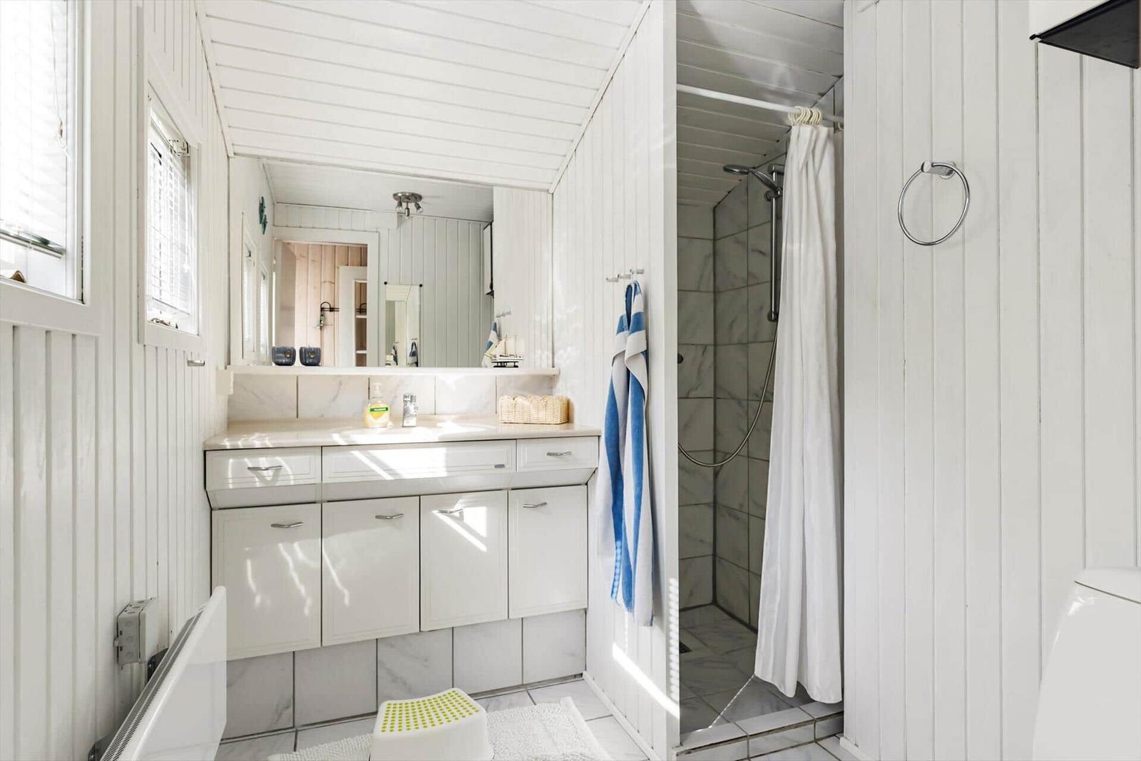 Badezimmer mit Dusche, Waschbecken und Spiegel. Weiße Holzwände und Fliesen.