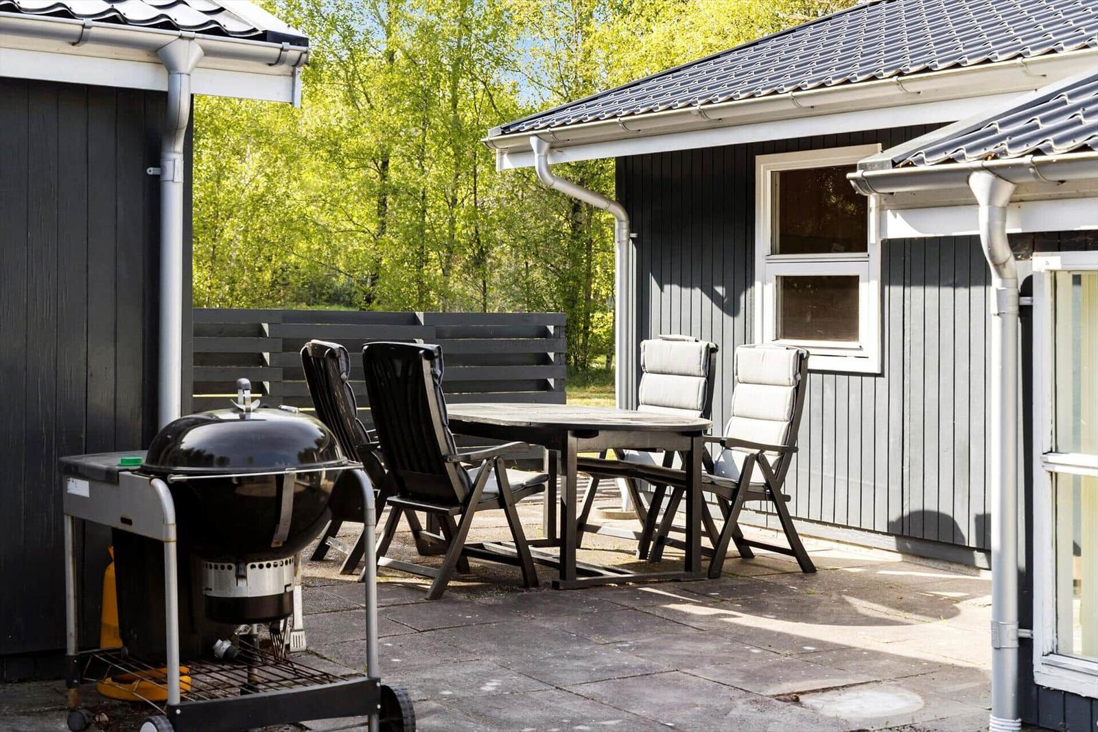 Terrasse mit Tisch, Stühlen und Grill vor einem Haus.