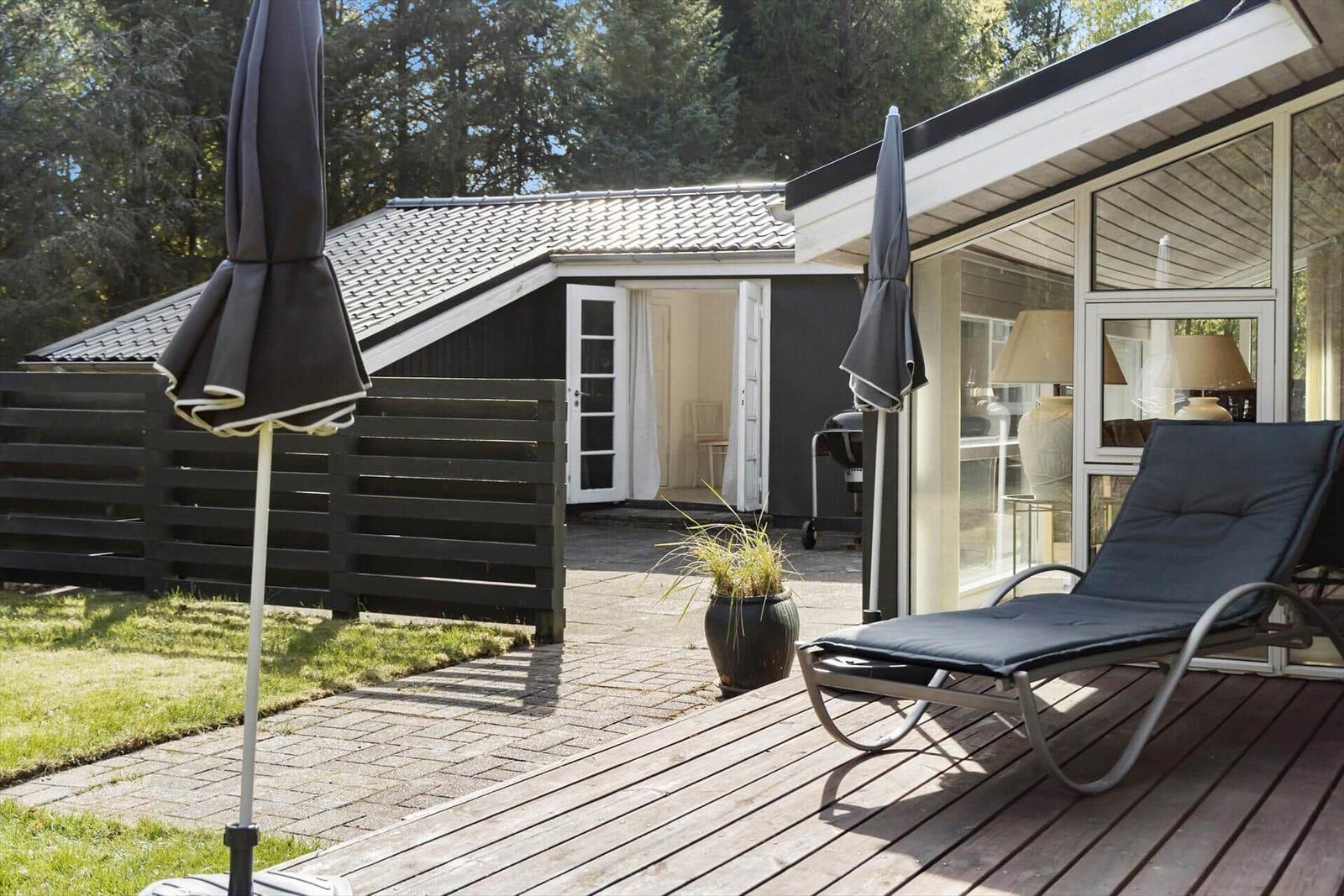 Terrasse mit Liegestuhl und geschlossenen Sonnenschirmen neben einem Haus mit Glasfront.
