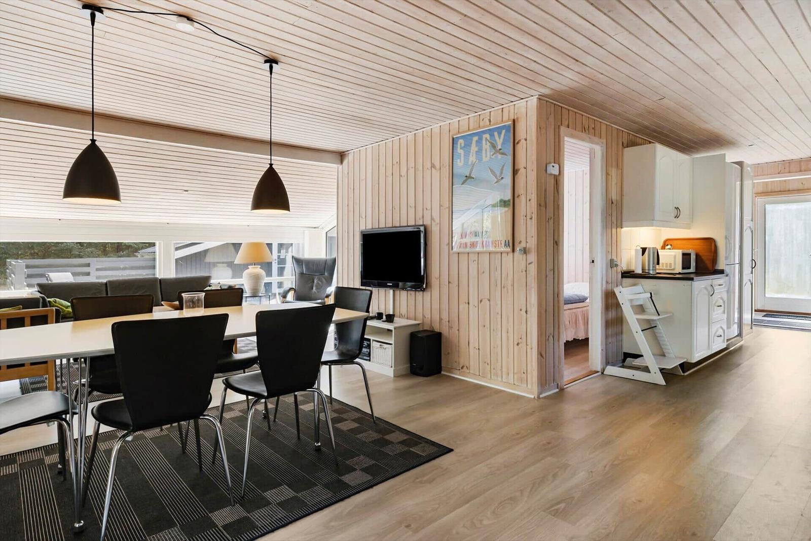 Wohnküche mit Essbereich, Fernseher und Schlafzimmer im Hintergrund.