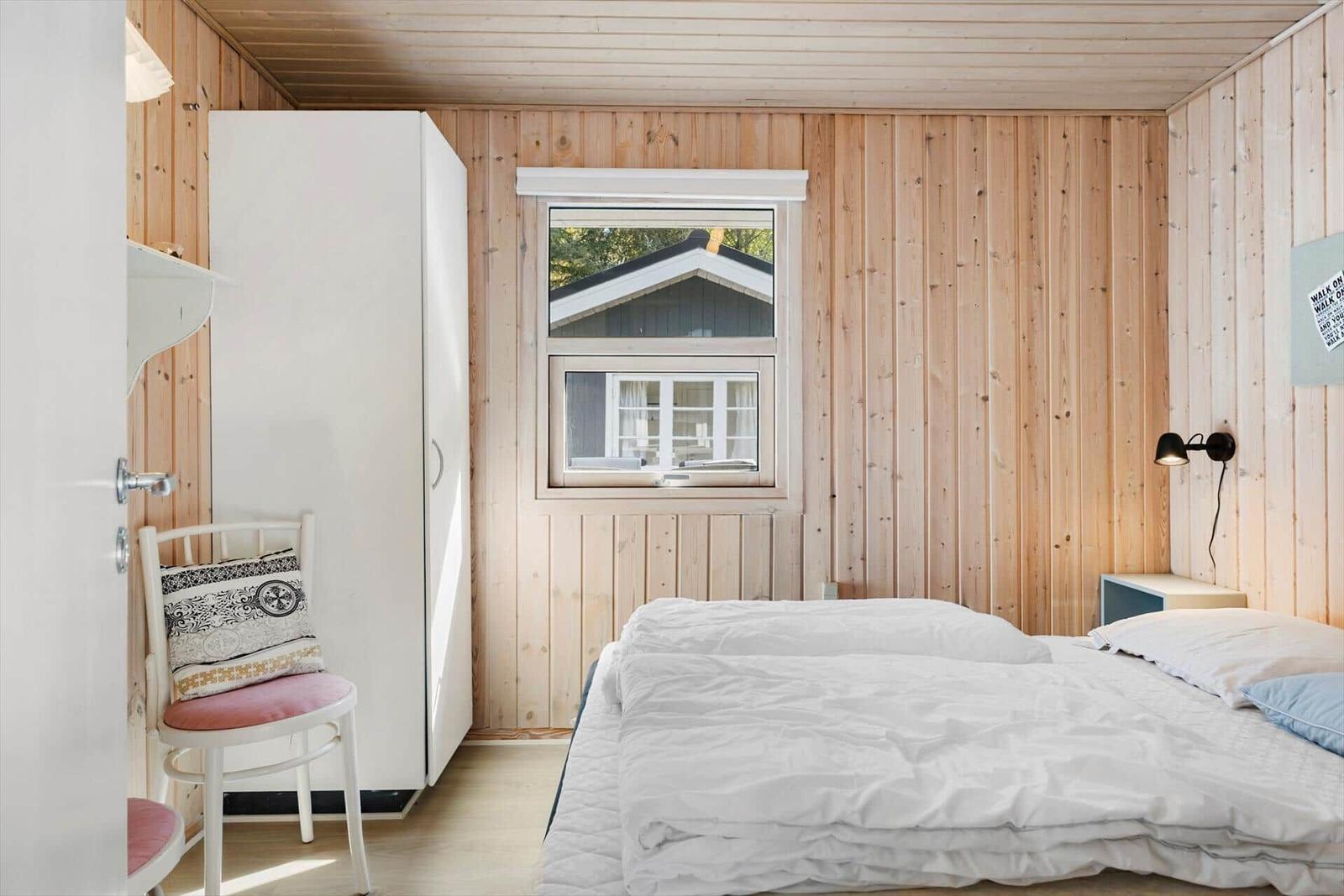 Schlafzimmer mit Holzwand, Bett, Kleiderschrank und Fenster mit Blick auf Haus.