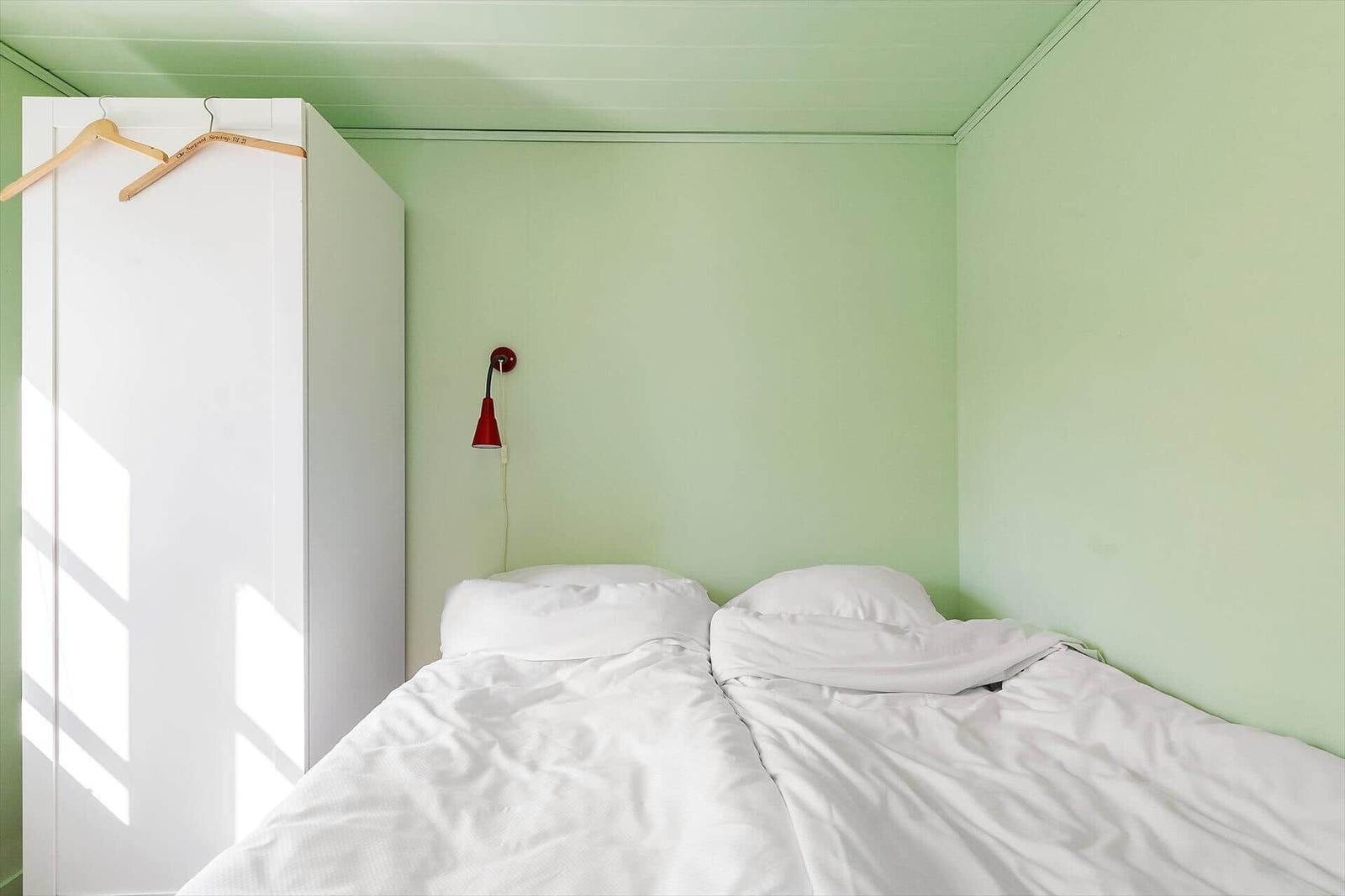 Schlafzimmer mit Bett, Kleiderschrank und Wandlampe.