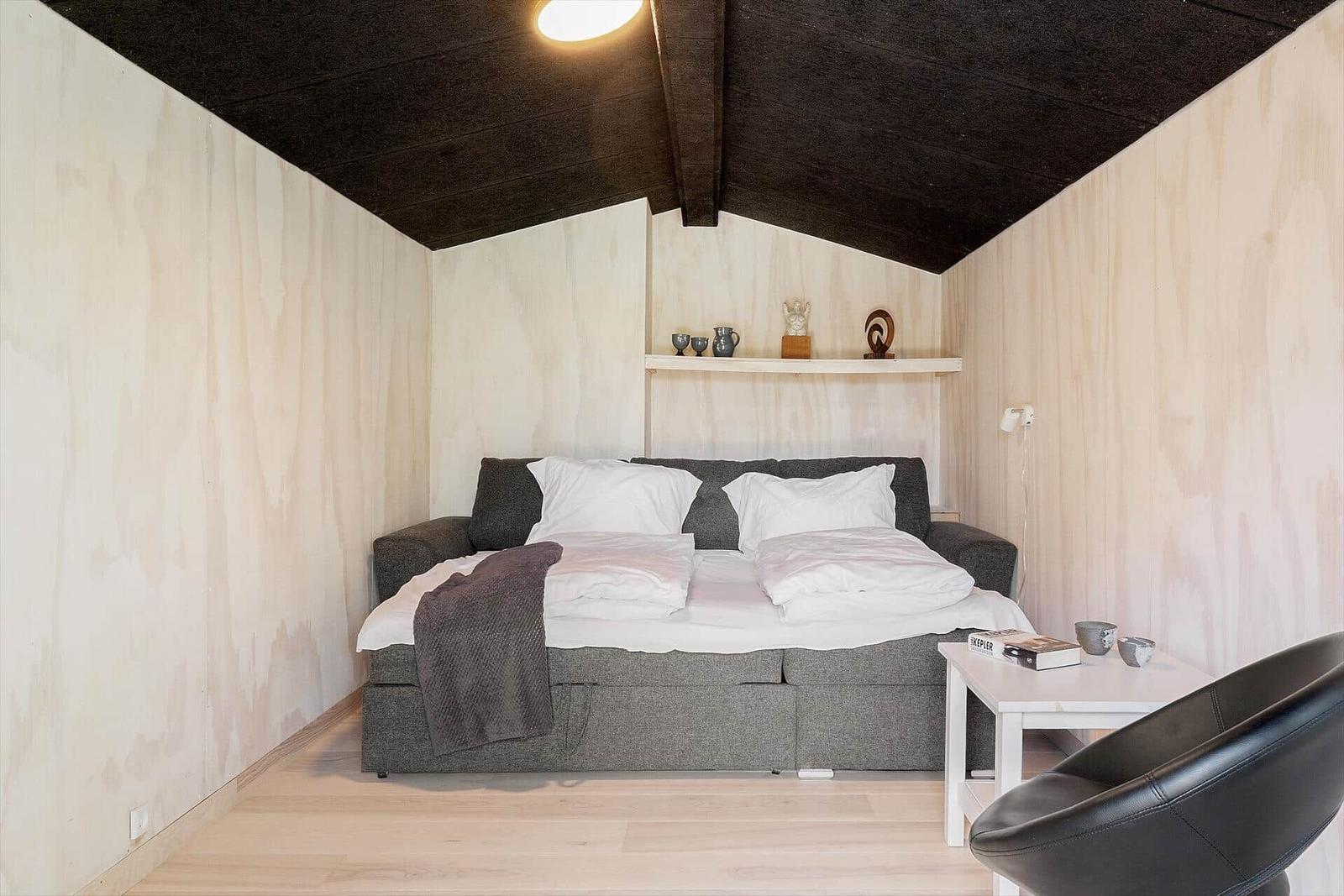 Schlafzimmer mit Bett, Nachttisch und Sessel unter schwarzem Dach
