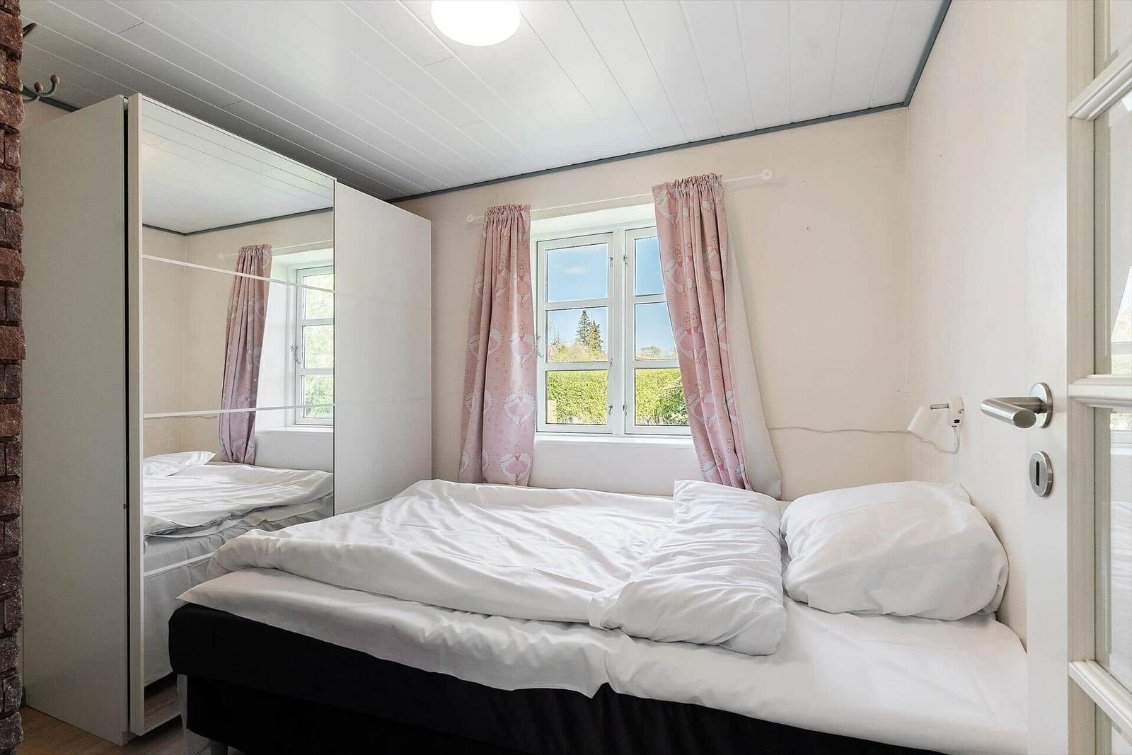 Schlafzimmer mit Bett, Fenster und Schrank. Vorhang und Decke sind rosa.