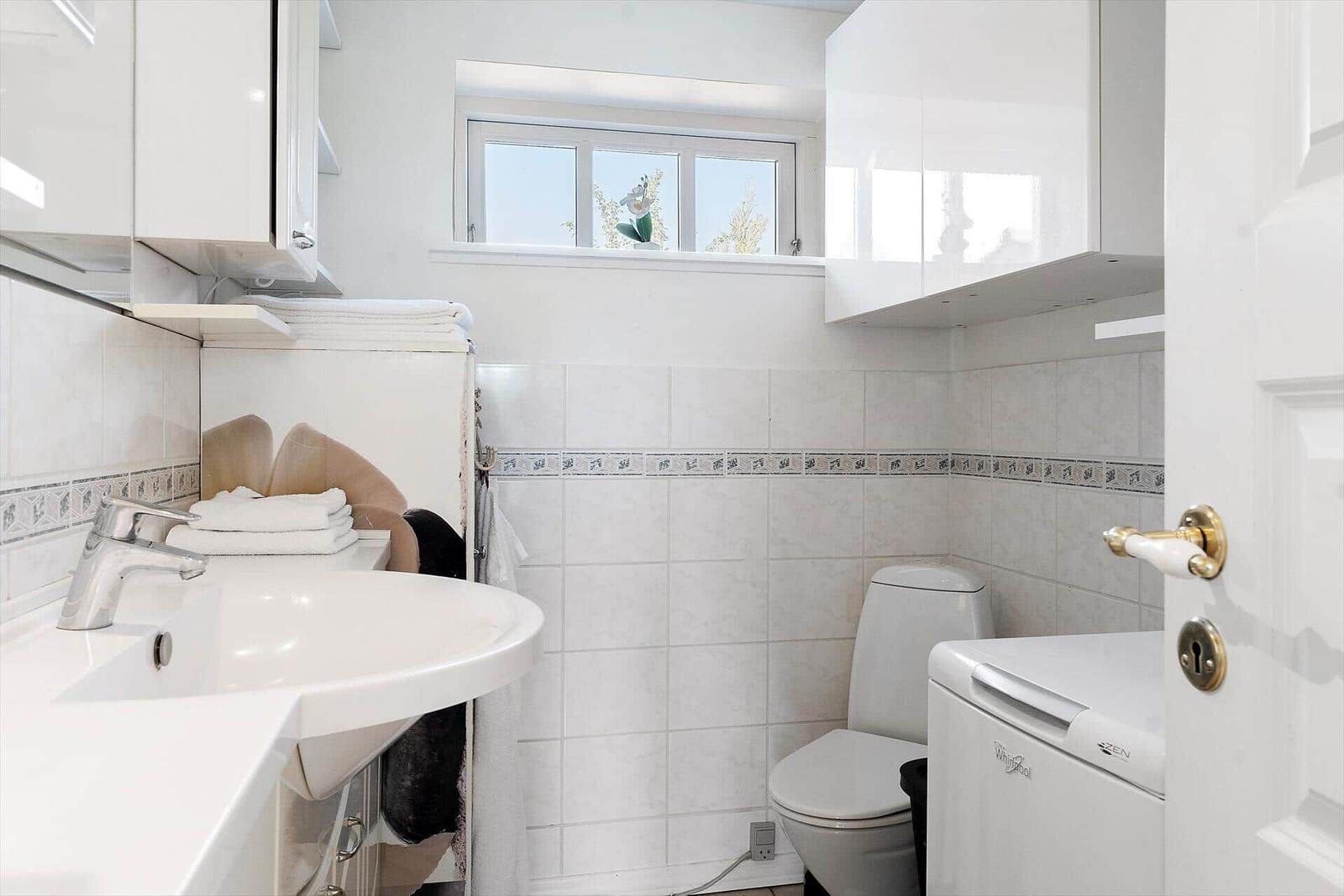 Badezimmer mit Waschbecken, Toilette und Waschmaschine. Fenster mit Blick nach draußen.