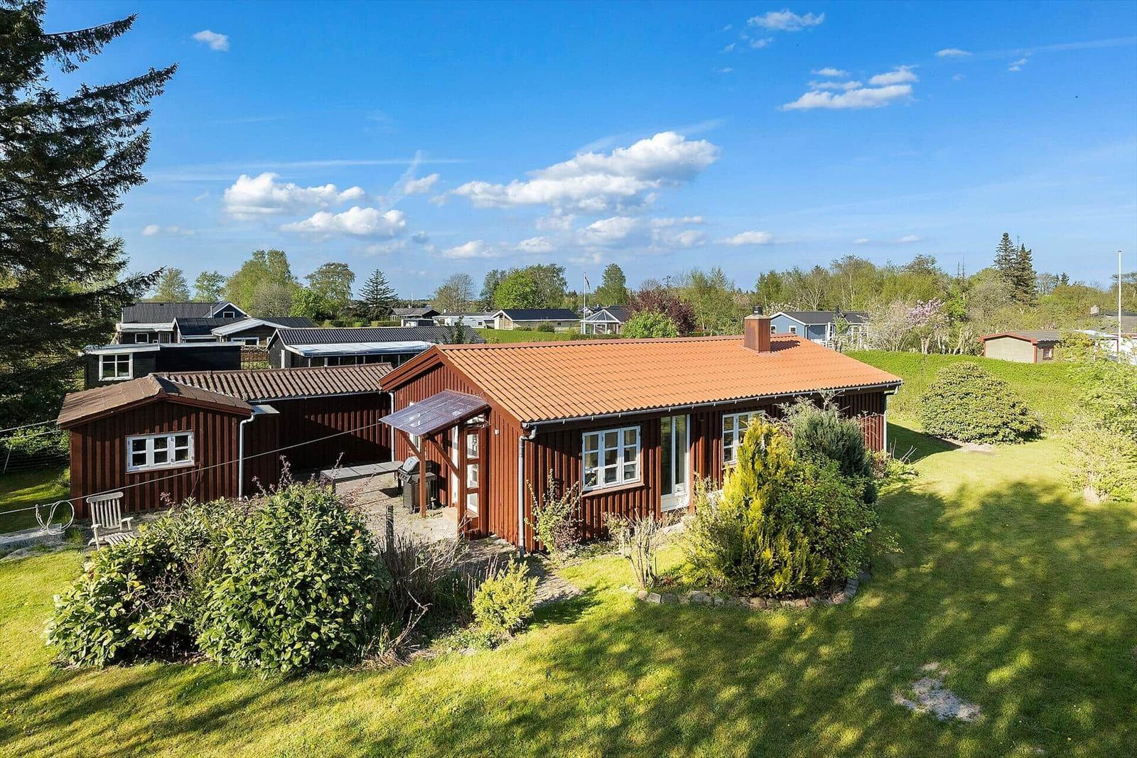 Holzhaus mit rotem Dach und Garten. Umgeben von Bäumen und Gras.