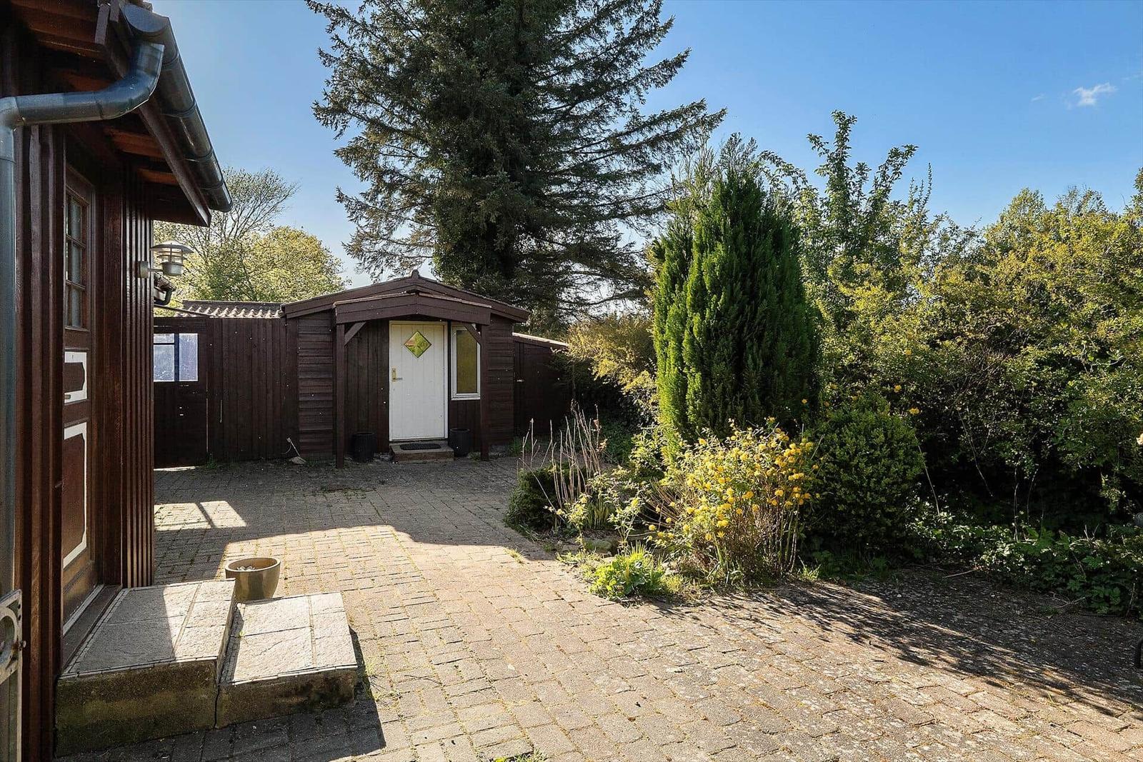 Pflasterweg führt zu einem Holzhaus mit weißer Tür und grüner Umgebung.