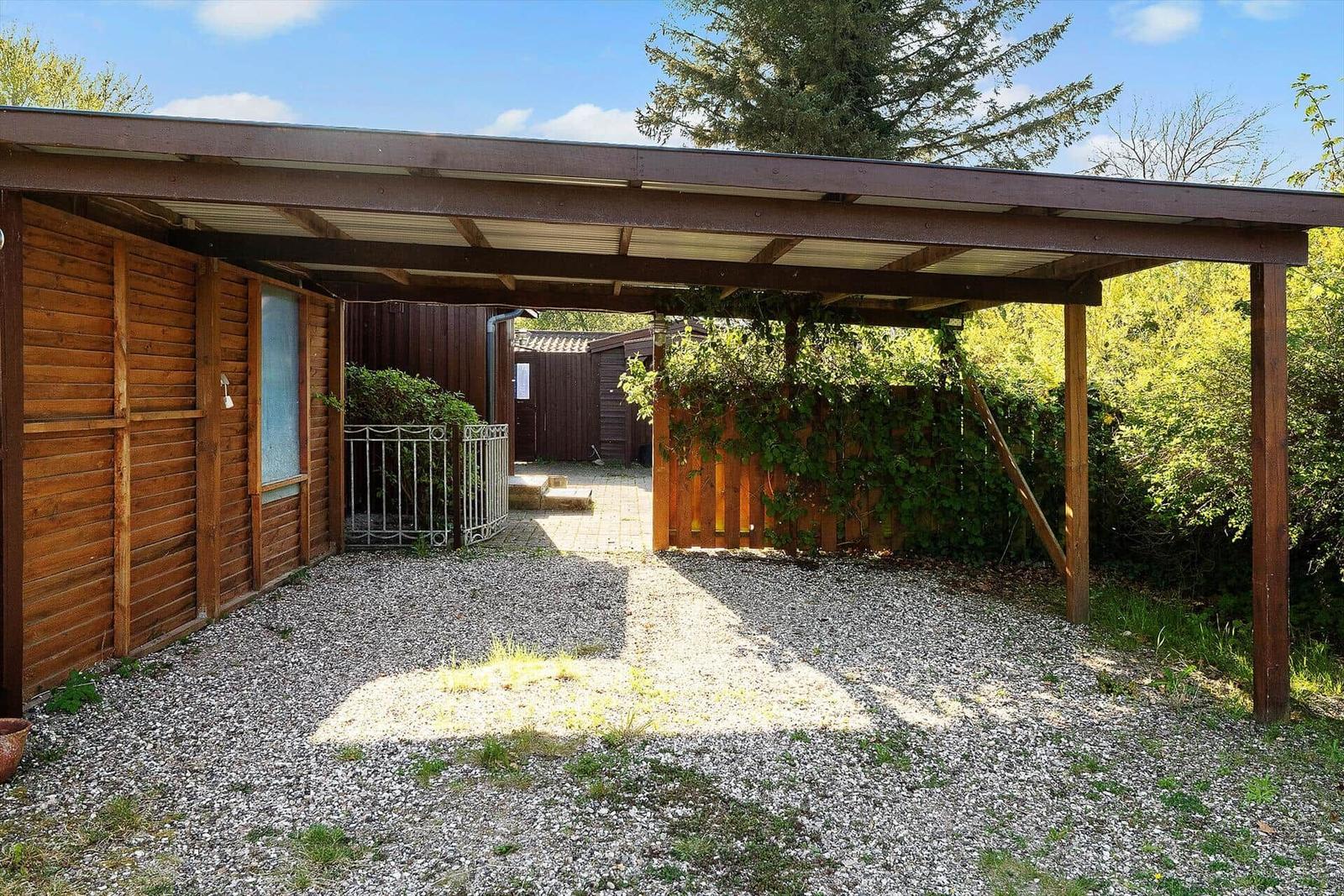 Holzüberdachung mit Kiesfläche und Gartenzaun im Hintergrund.