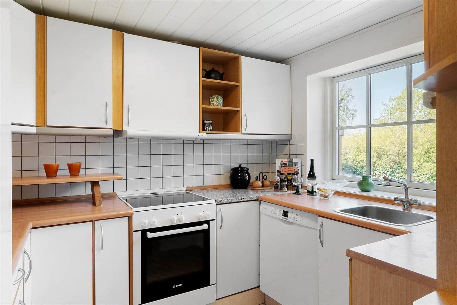 Küche mit weißen Schränken, Holzoberflächen und Fensterblick auf Grün.