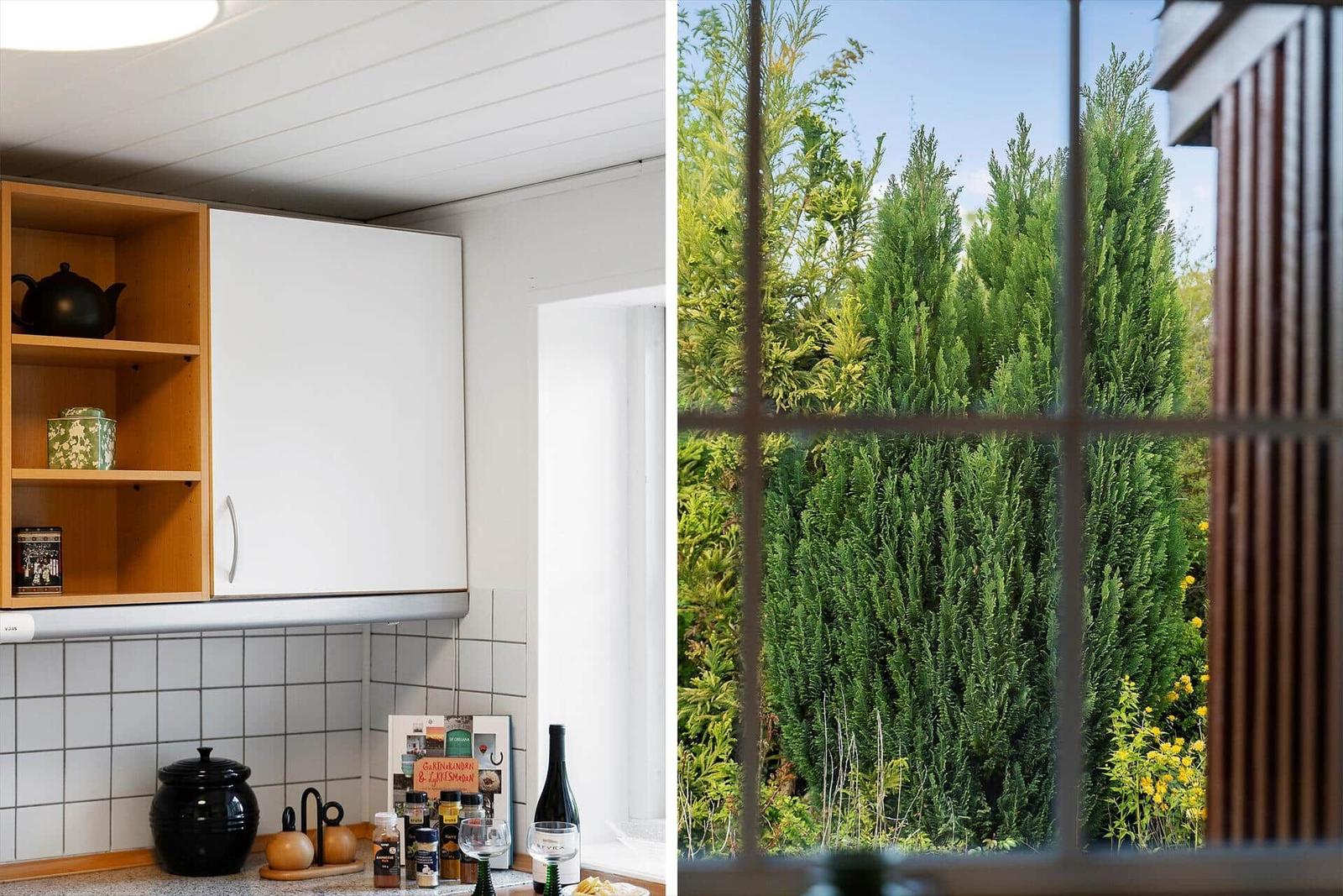 Küche mit Holz- und weißen Schränken. Blick auf grüne Hecken durch Fenster.