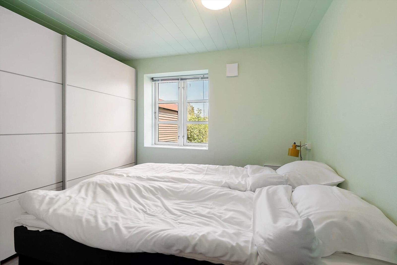 Schlafzimmer mit Bett, Fenster und Schrank. Decke mit Holzverkleidung.
