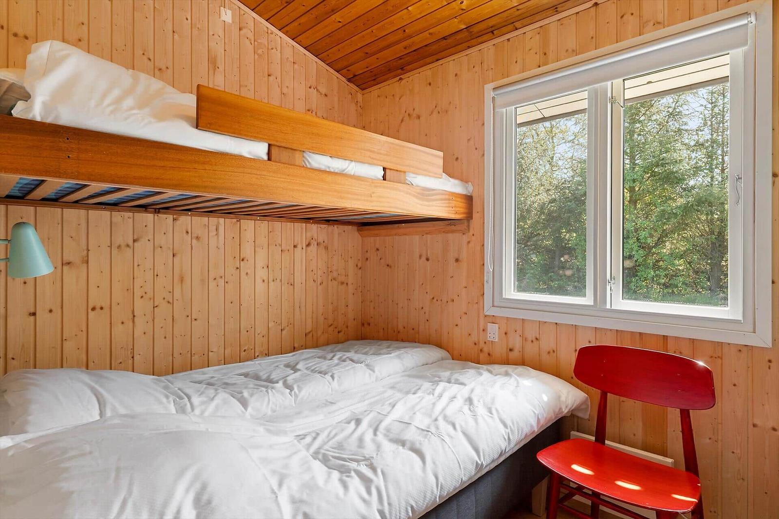 Zimmer mit Schlafcouch und obere Schlafcouch, roter Stuhl und Fenster mit Blick auf Wald.