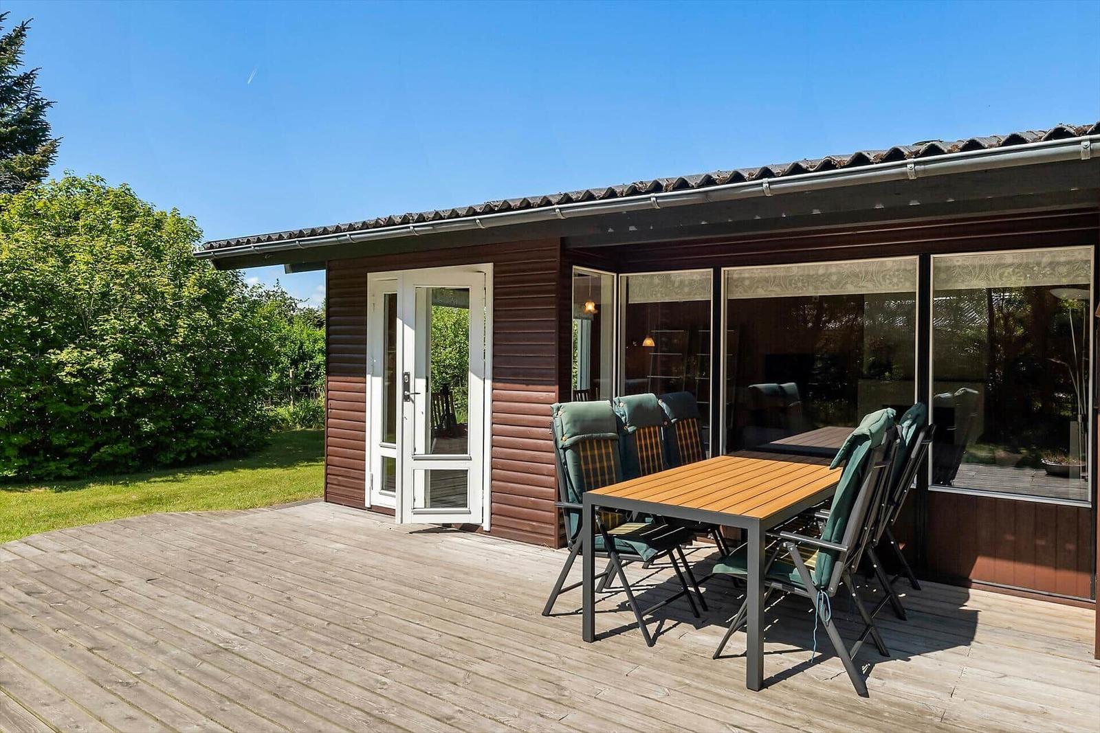 Terrasse mit Tisch und Stühlen vor einem Haus mit Holzfassade und Glasfront.
