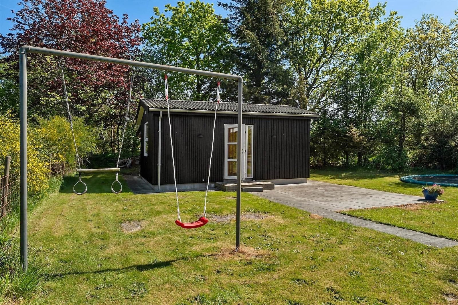 Schwarzes Gartenhaus mit Spielgerüst und Rutsche im grünen Garten.