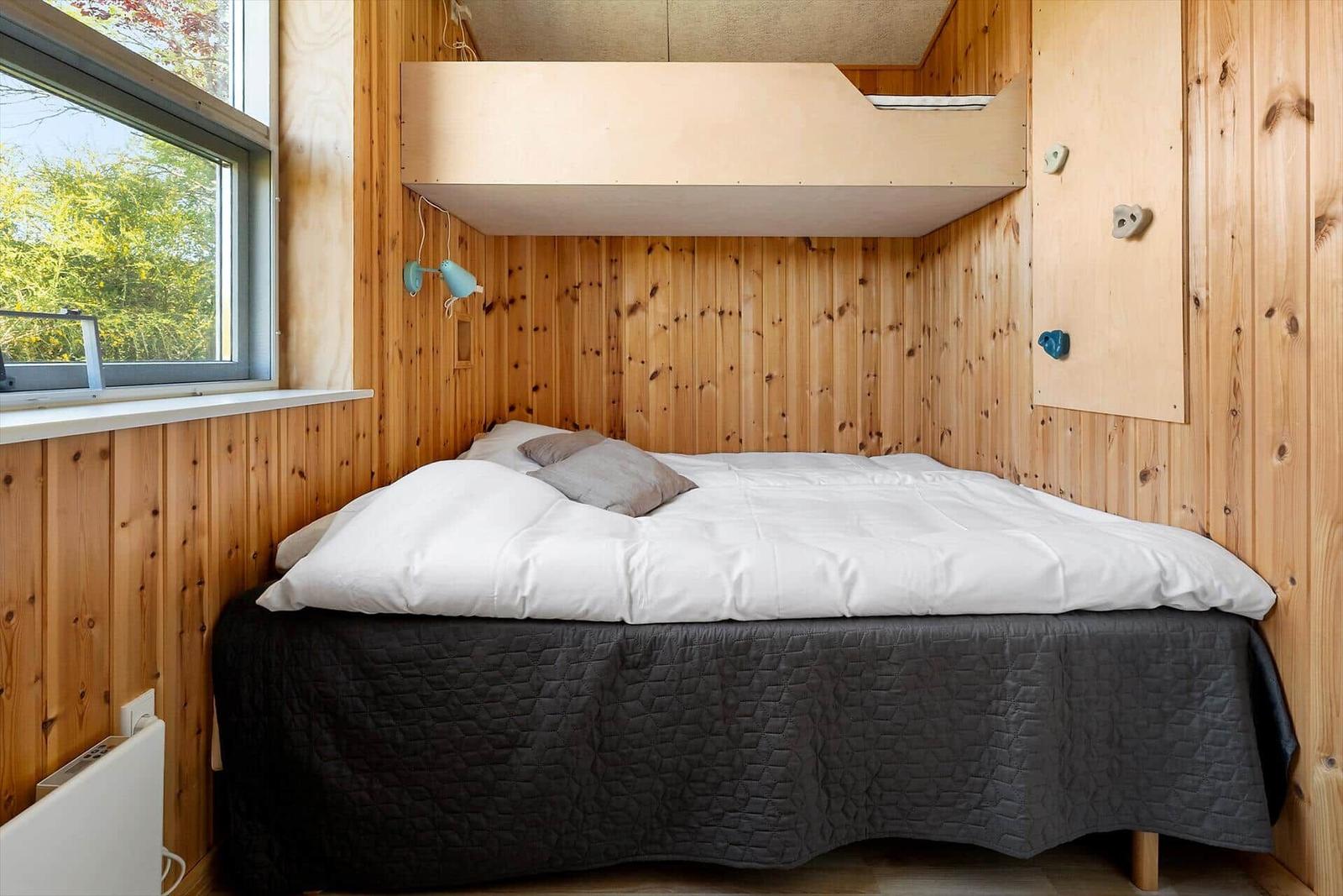 Schlafzimmer mit Doppelbett, Holzwand und Fenster. Oben Schlafplatz mit Kletterwand.