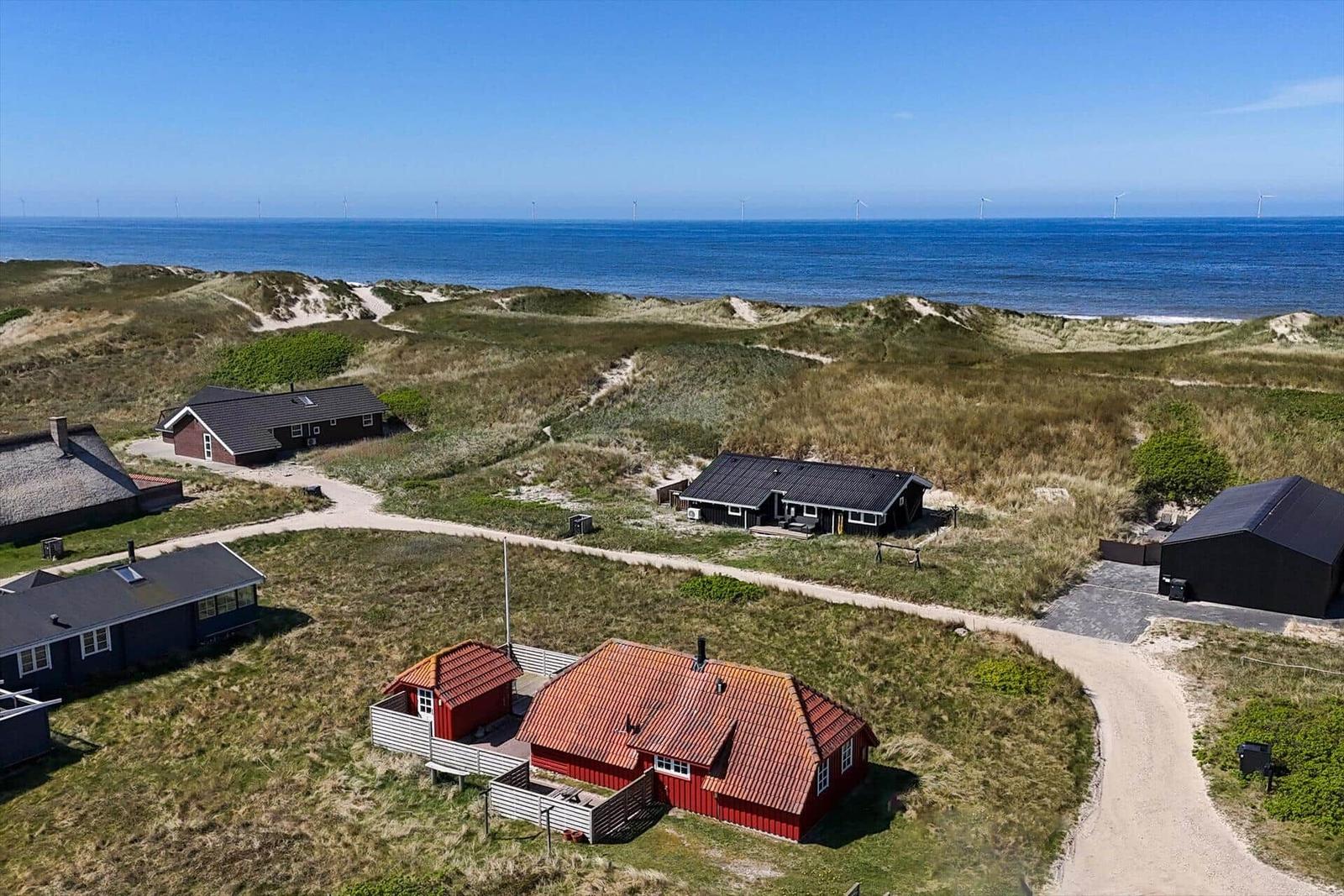 Rote Häuser auf Dünen mit Blick auf das Meer und Windkraftanlagen