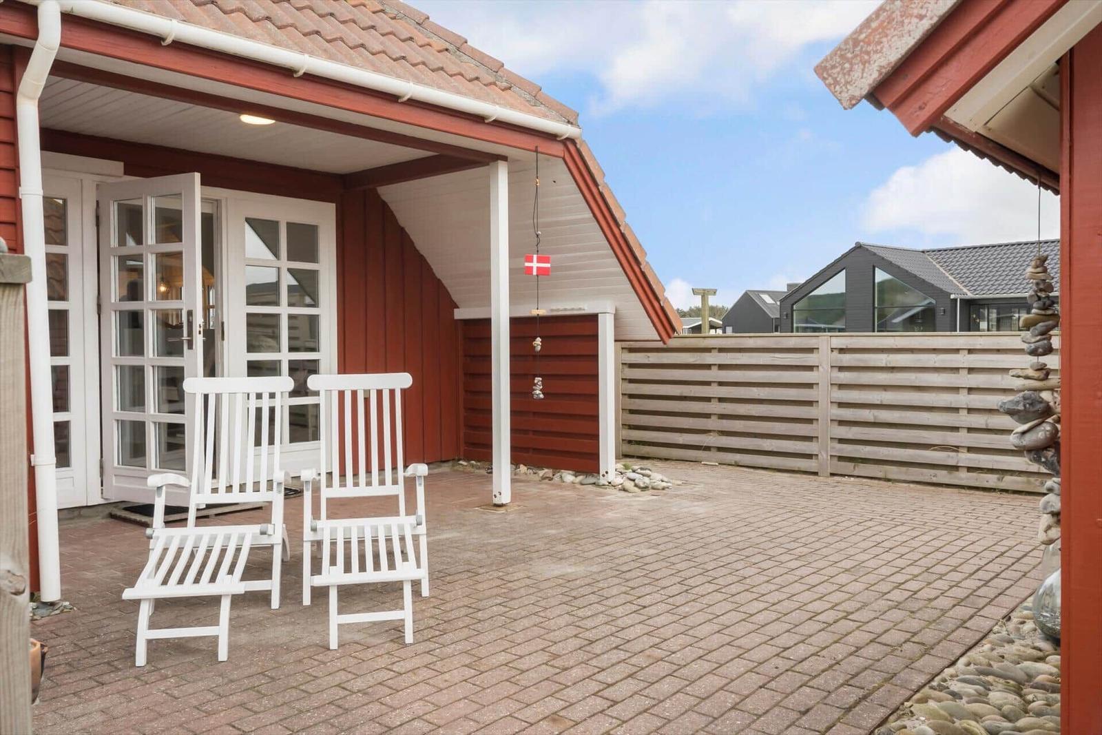 Terrasse mit zwei weißen Stühlen vor rotem Haus mit Dach und Fenstern.