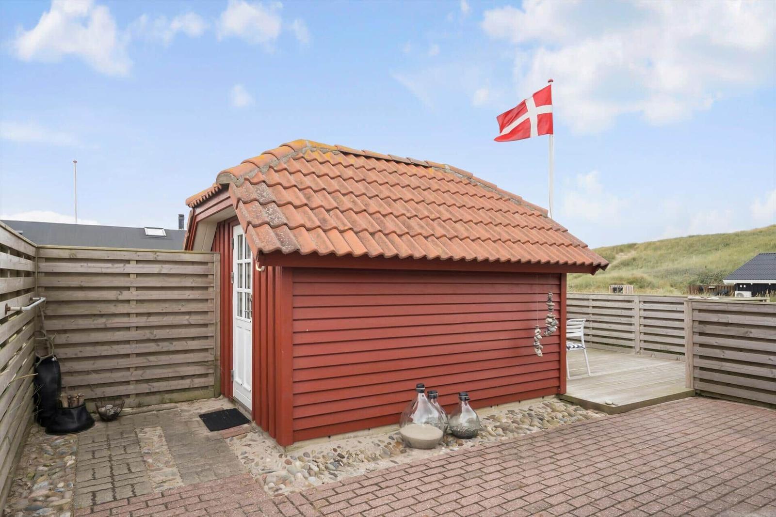 Rotes Holzhaus mit Terrasse und dänischer Flagge. Holzumzäunung und Steinplatten.