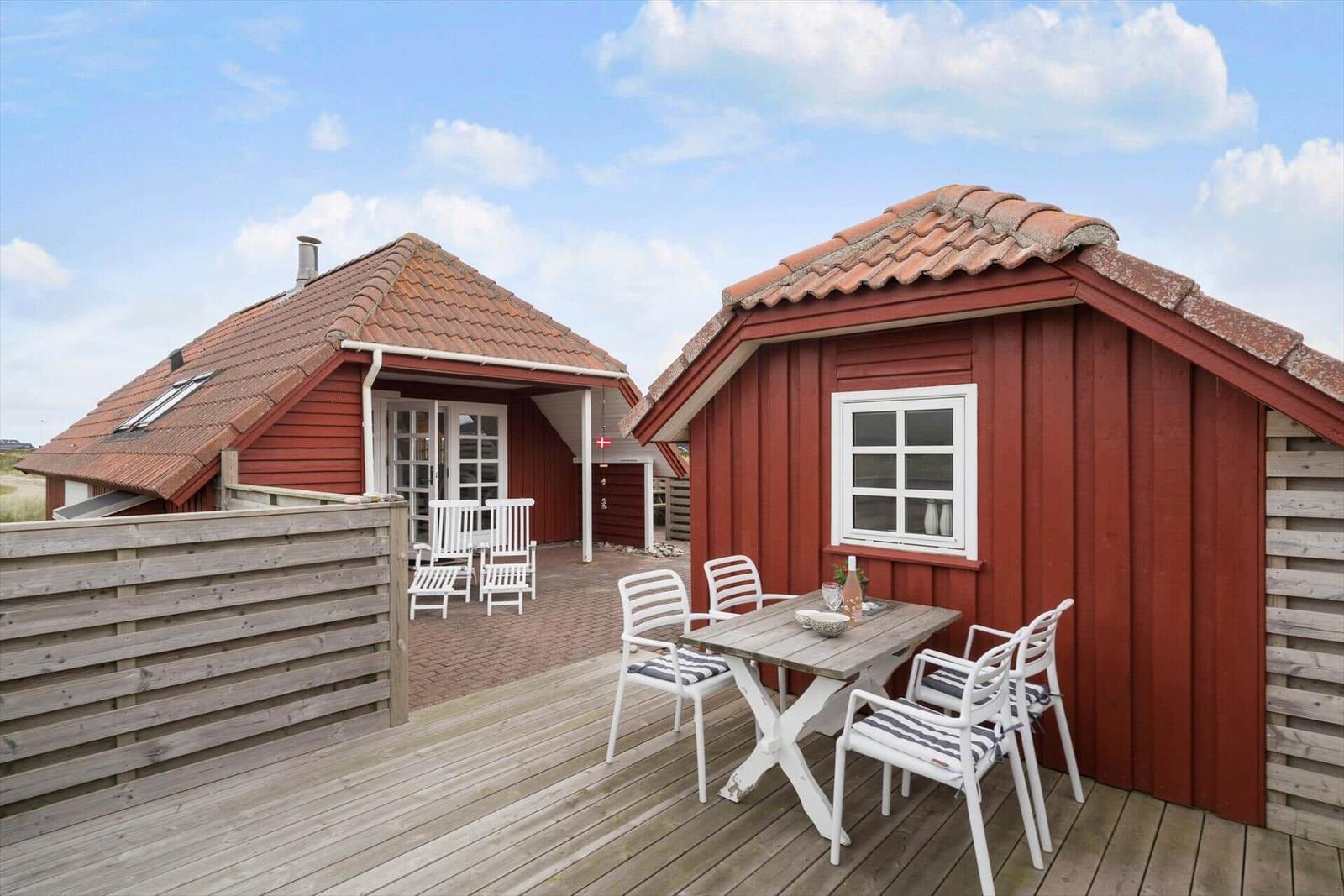Rote Holzhäuser mit Terrasse und Tisch. Weiße Stühle und Holzdecke.