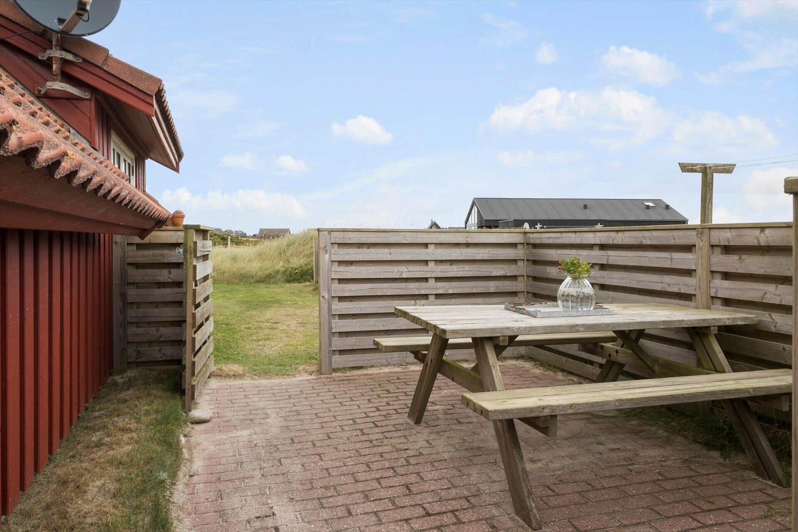 Terrasse mit Holztisch und Bänken, umgeben von Holzgeländer und Grasfläche.