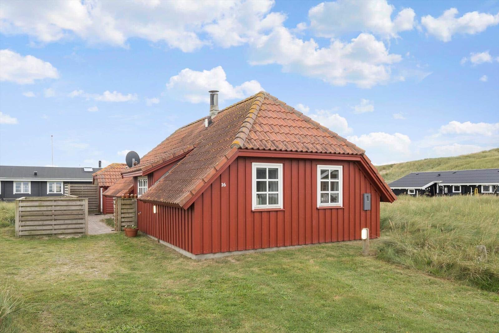 Rotes Holzhaus mit Schieferdach und weißen Fenstern in grüner Umgebung.