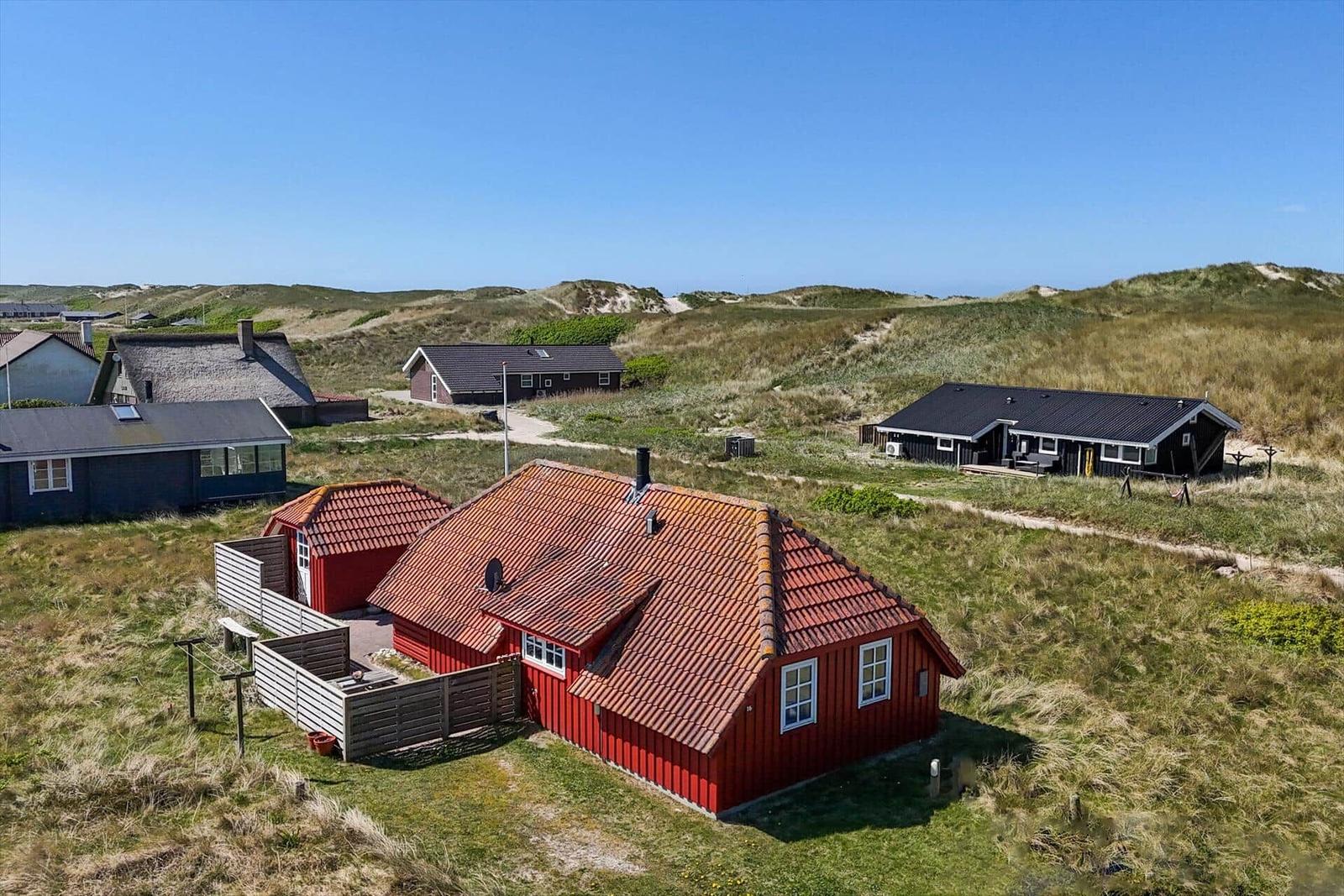 Rotes Haus mit rotem Dach in einer grünen Landschaft mit weiteren Häusern.