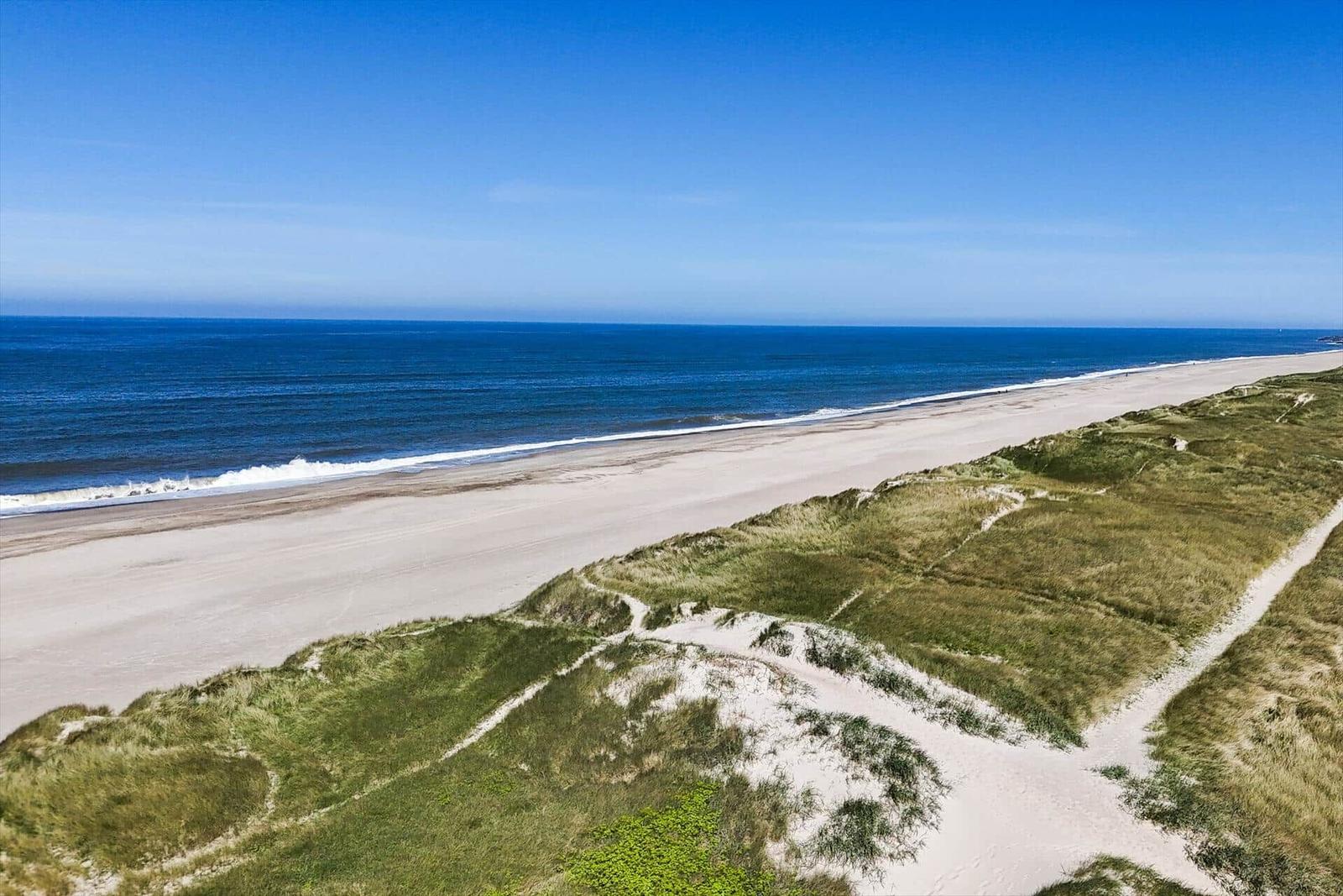 Strand mit Dünen und blauem Meer unter klarem Himmel.