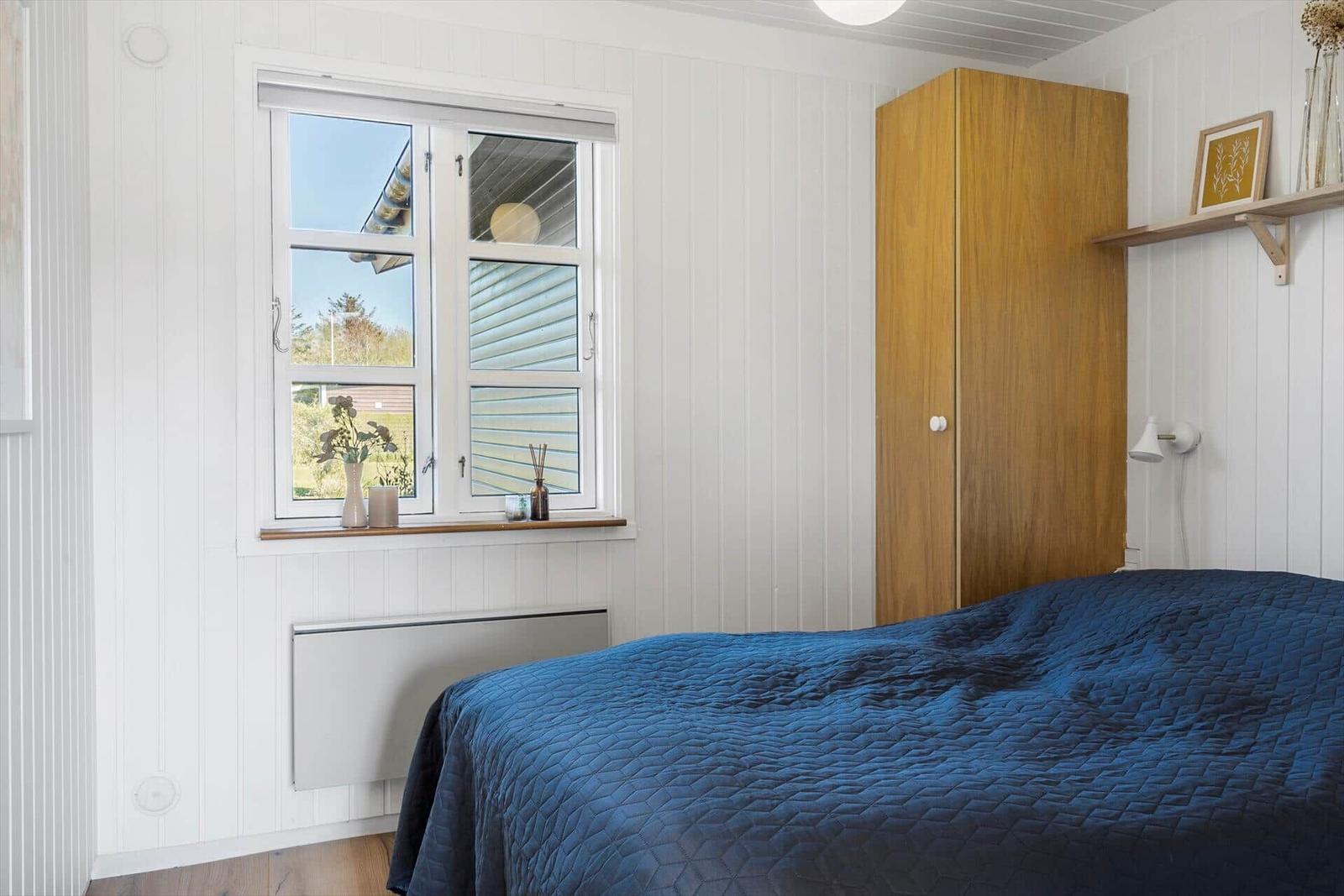 Bedroom with blue bed, wooden wardrobe, and window overlooking outside.
