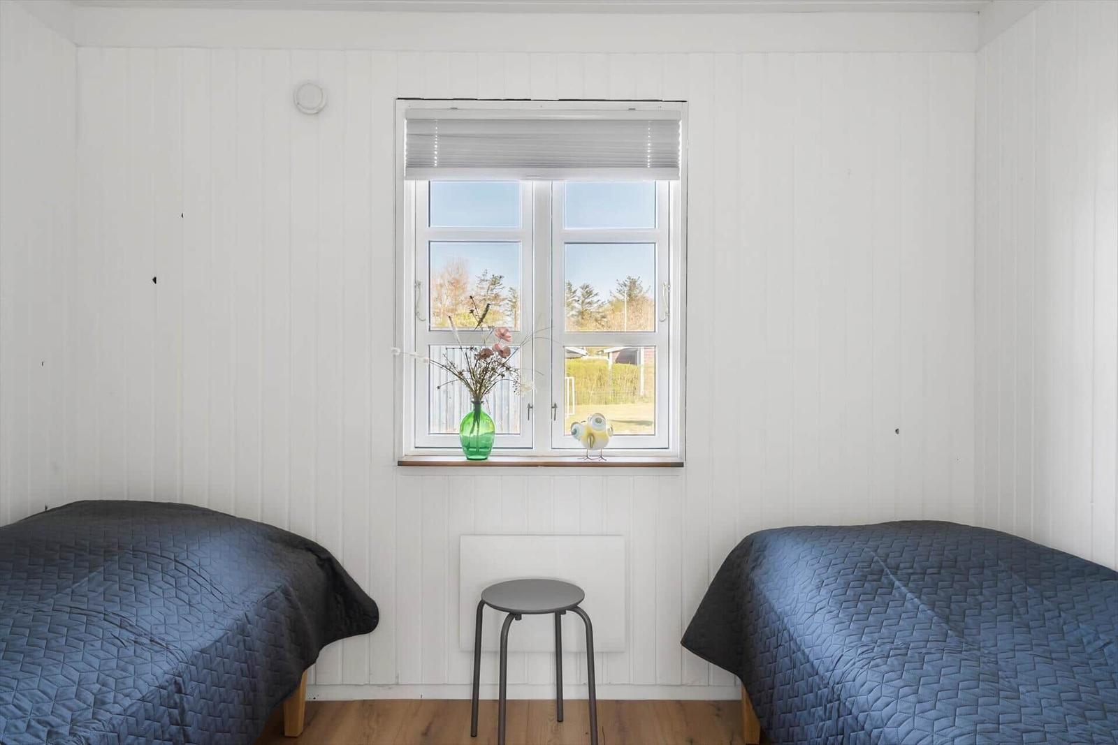 Two beds with dark blue covers are in a room with white wall paneling and a window.