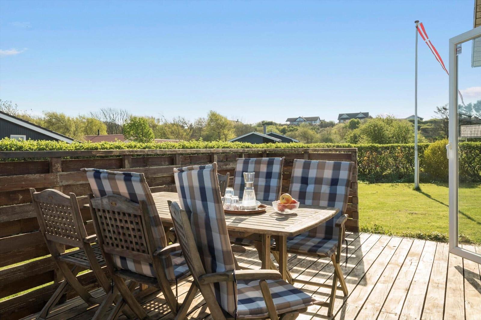 Deck with wooden table and chairs, view of green landscape and flag.