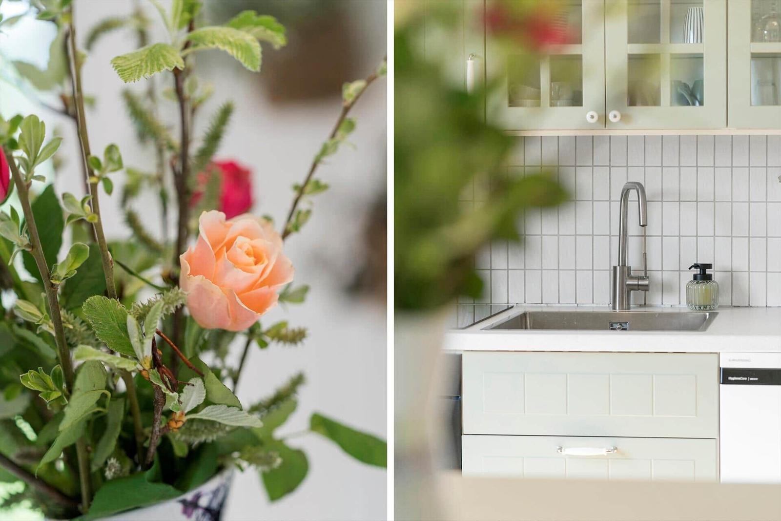 Kitchen with white countertop and stainless steel sink. Bouquet with pink rose in foreground.