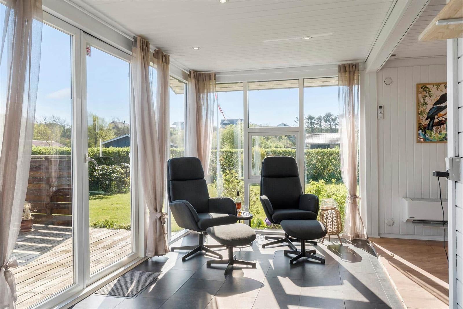 Two black chairs with footstools stand before large windows. Outside is a terrace with garden.