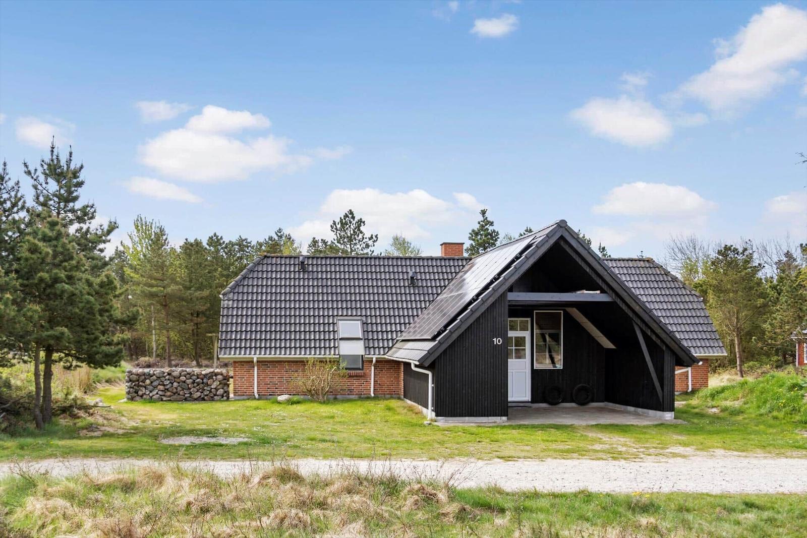 Haus mit dunklem Holz und Ziegelfassade, umgeben von Gras und Bäumen unter blauem Himmel.