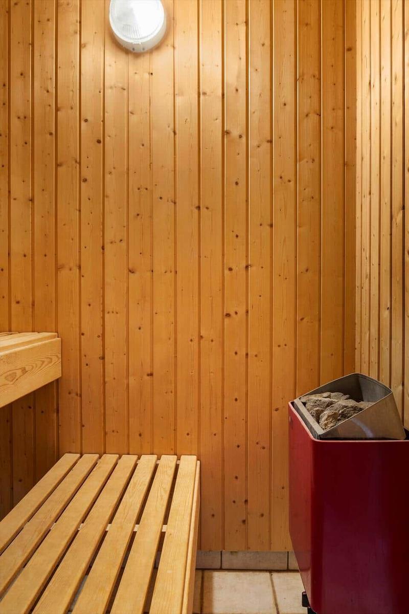Sauna mit Holzwand, Sitzbank und rotem Heizofen.