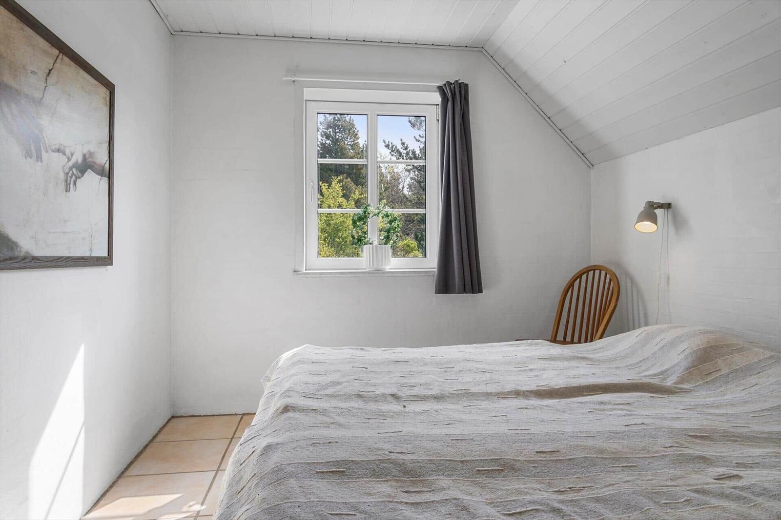 Schlafzimmer mit Bett, Fenster und Stuhl. Wandbild und Lampe sind sichtbar.