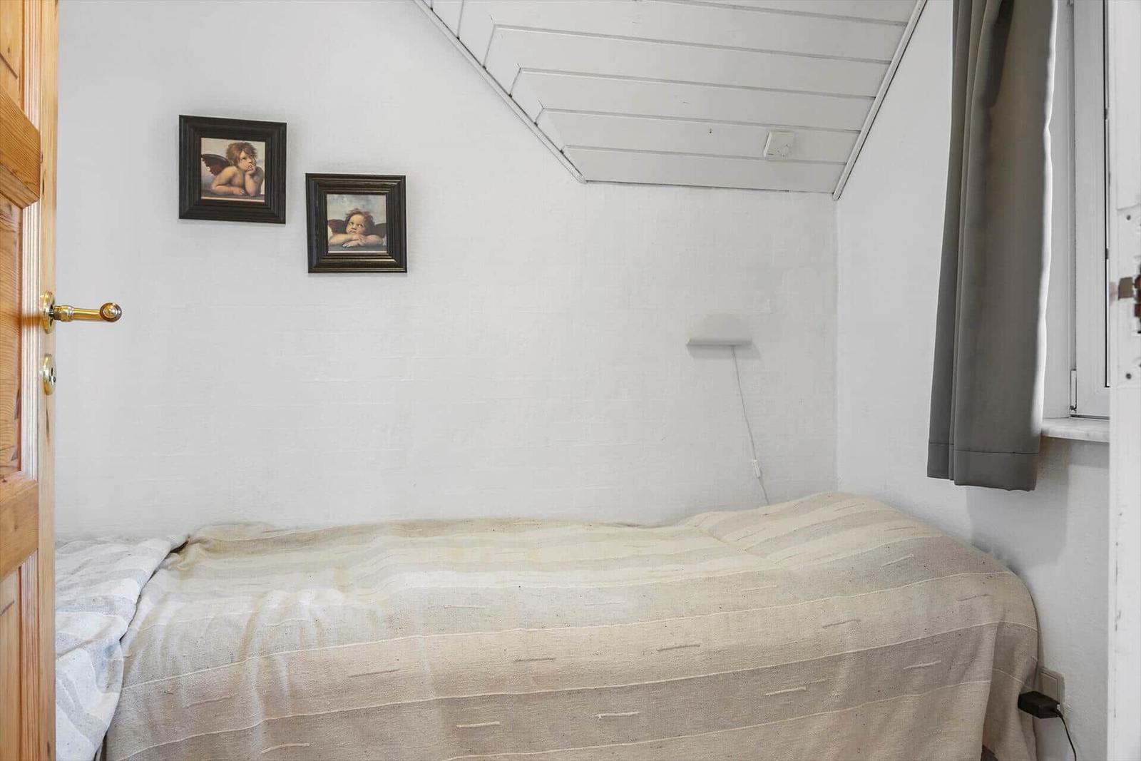 Ein Schlafzimmer mit Bett, Wandbildern und Fenster mit Vorhang.